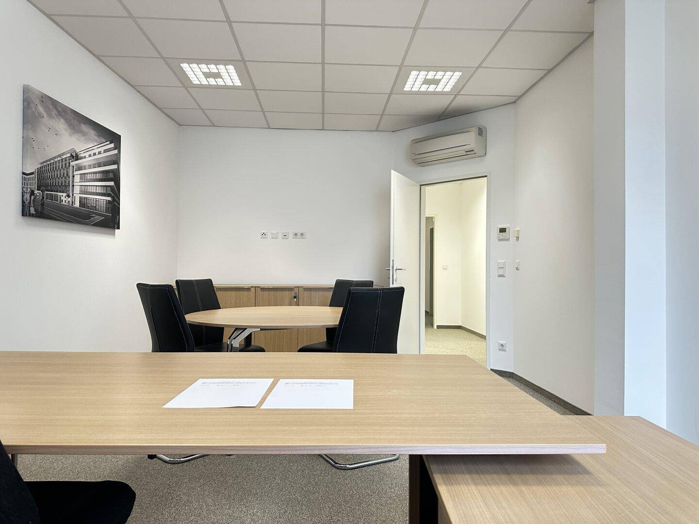 Modern eingerichtetes Büro mit Besprechungstisch, Stühlen und Klimaanlage, ideal für kleine Teams.