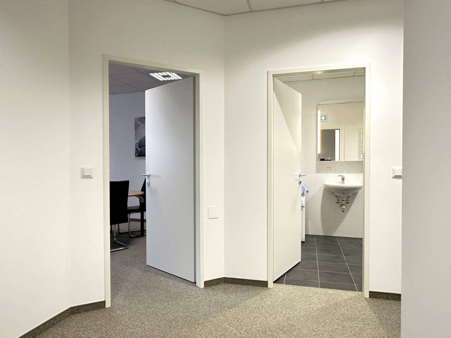 Flur mit Zugang zu einem Büro und einem Badezimmer, ausgestattet mit Teppichboden.