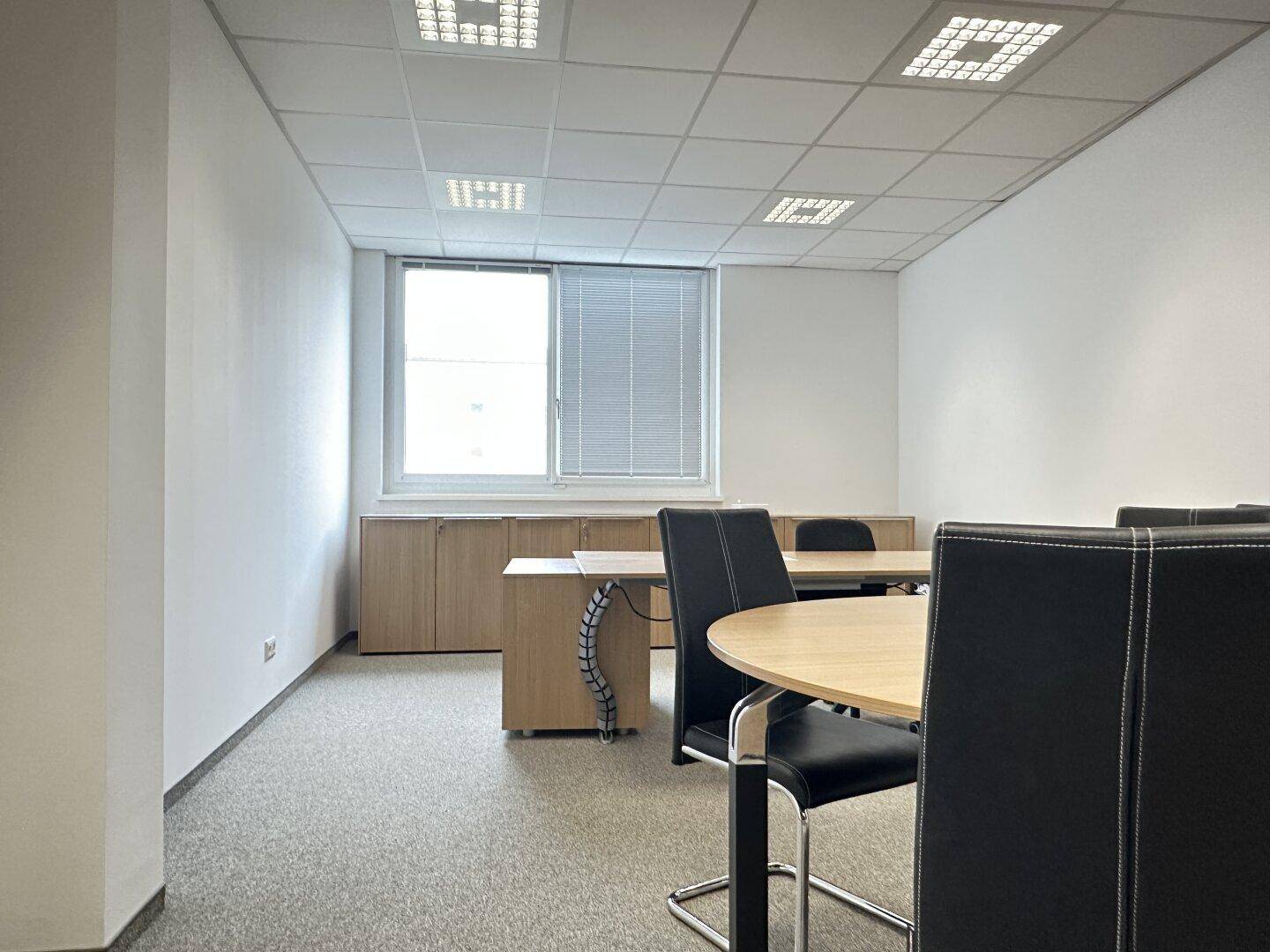Funktionales Büro mit Besprechungstisch, Stühlen und Holzschränken, ideal für konzentriertes Arbeiten.