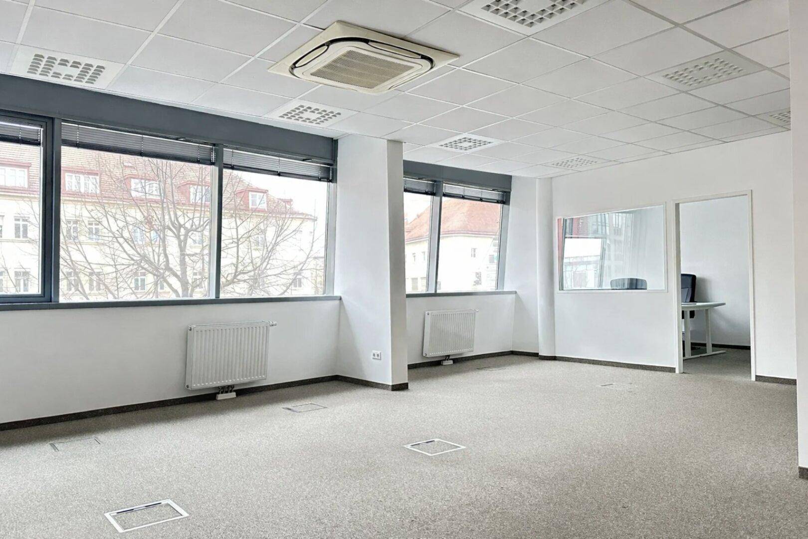 Geräumiges, leeres Büro mit Teppichboden, großen Fenstern und Klimaanlage, bereit zur individuellen Gestaltung.