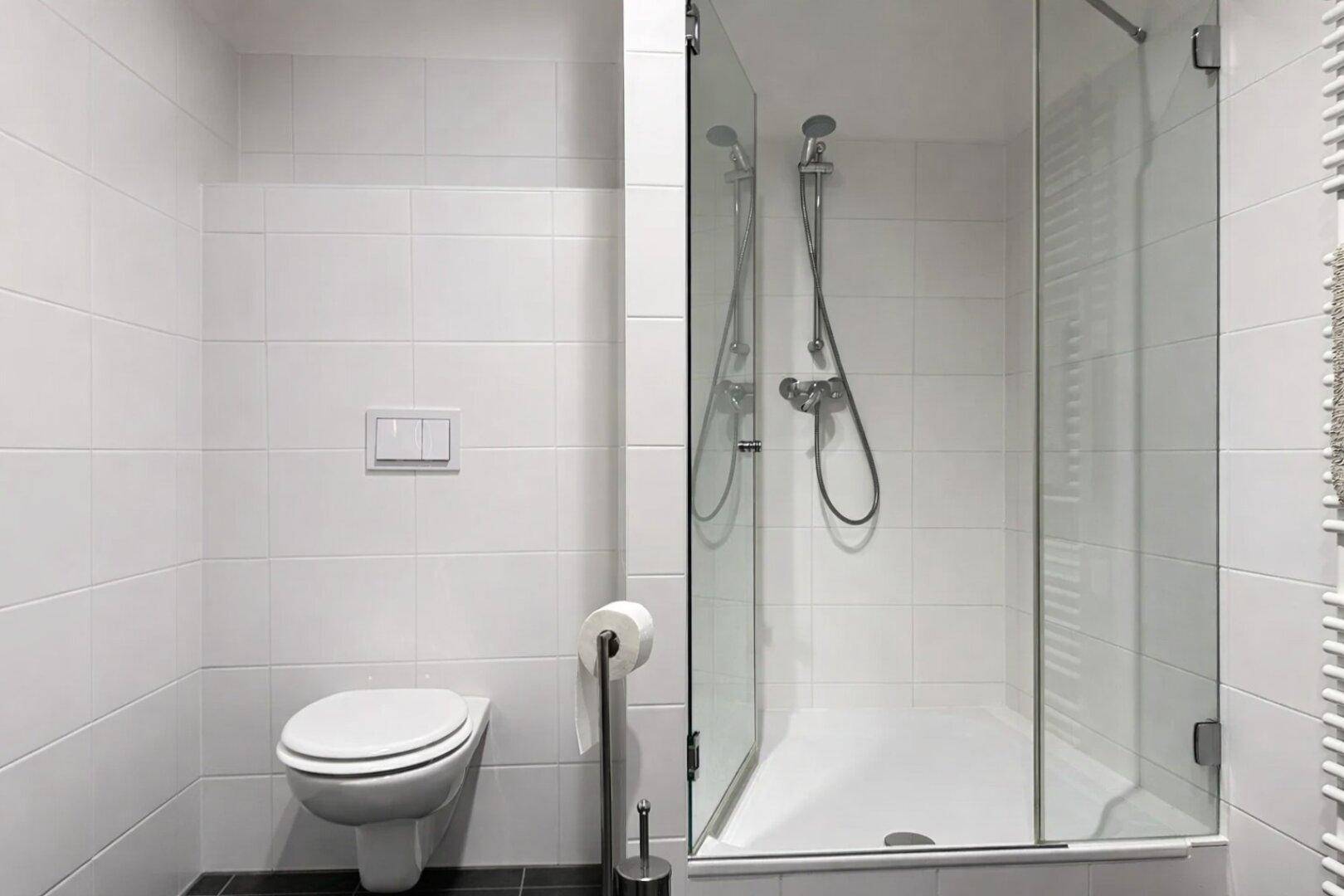 Modernes Badezimmer mit Toilette, Duschkabine und weißen Wandfliesen, sehr gepflegt.