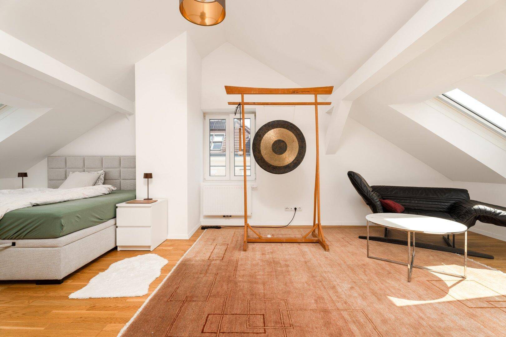 Helles Schlafzimmer im Dachgeschoss mit Dachschrägen, Holzboden und einem dekorativen Gong.