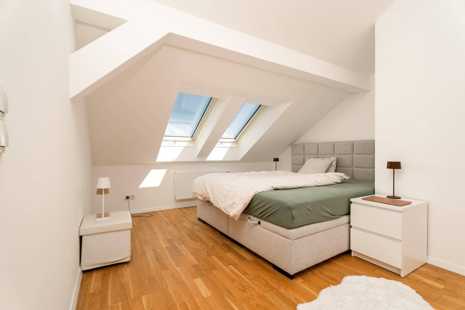 Modernes Schlafzimmer im Dachgeschoss mit Dachfenstern, Holzboden und minimalistischer Einrichtung.