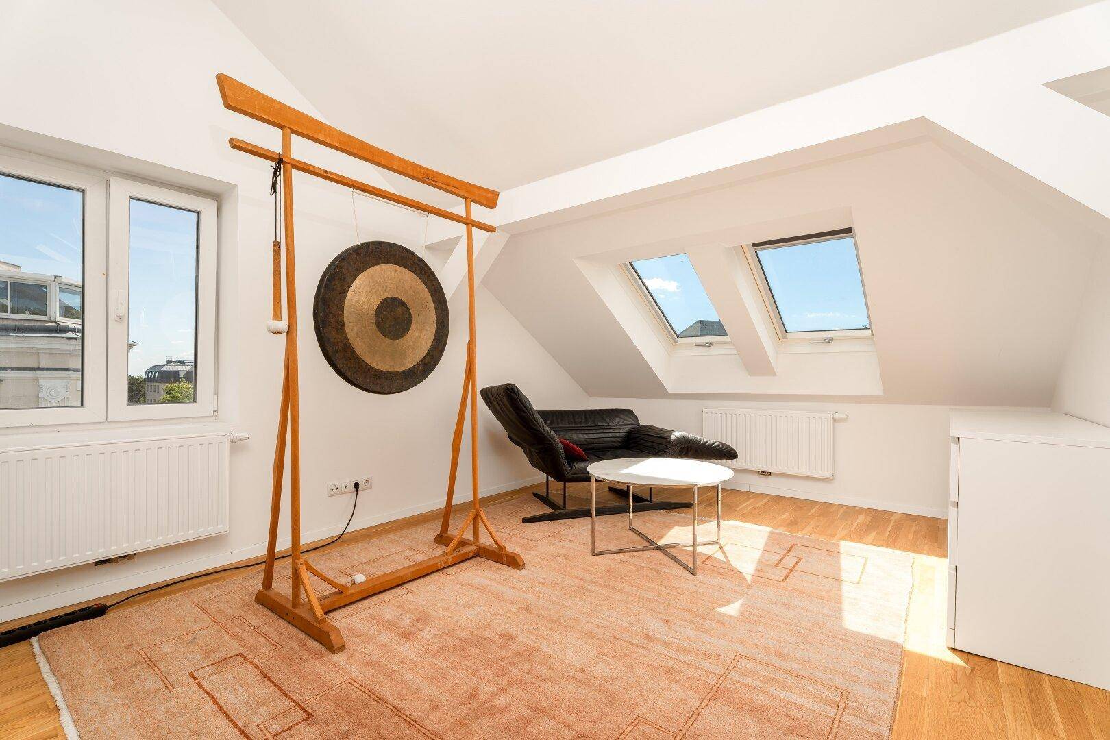 Geräumiges Dachgeschosszimmer mit Holzboden, Dachfenstern und einem bequemen Sessel.