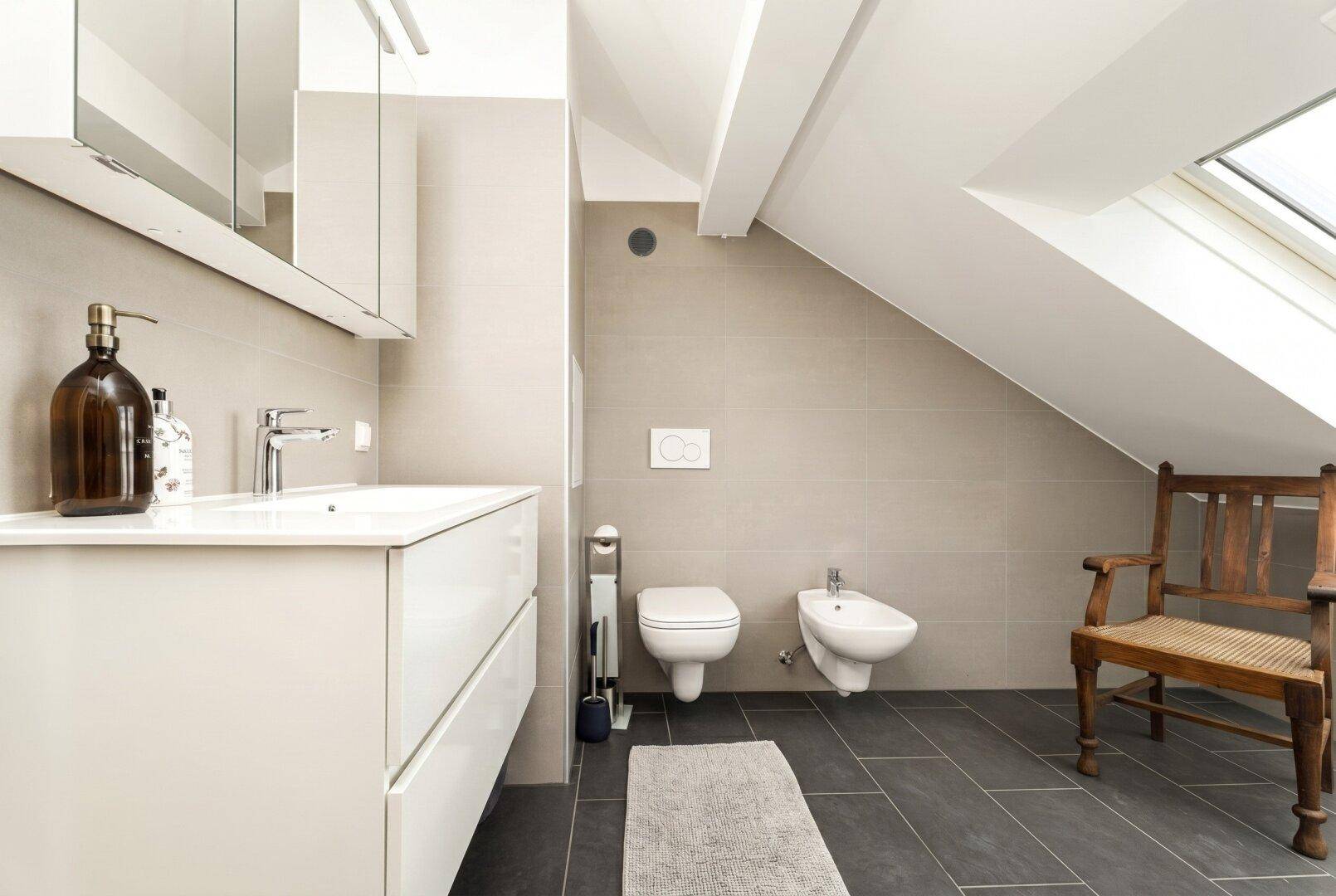 Modernes Badezimmer im Dachgeschoss mit Schrägen, dunklen Fliesen und wandhängendem WC und Bidet.