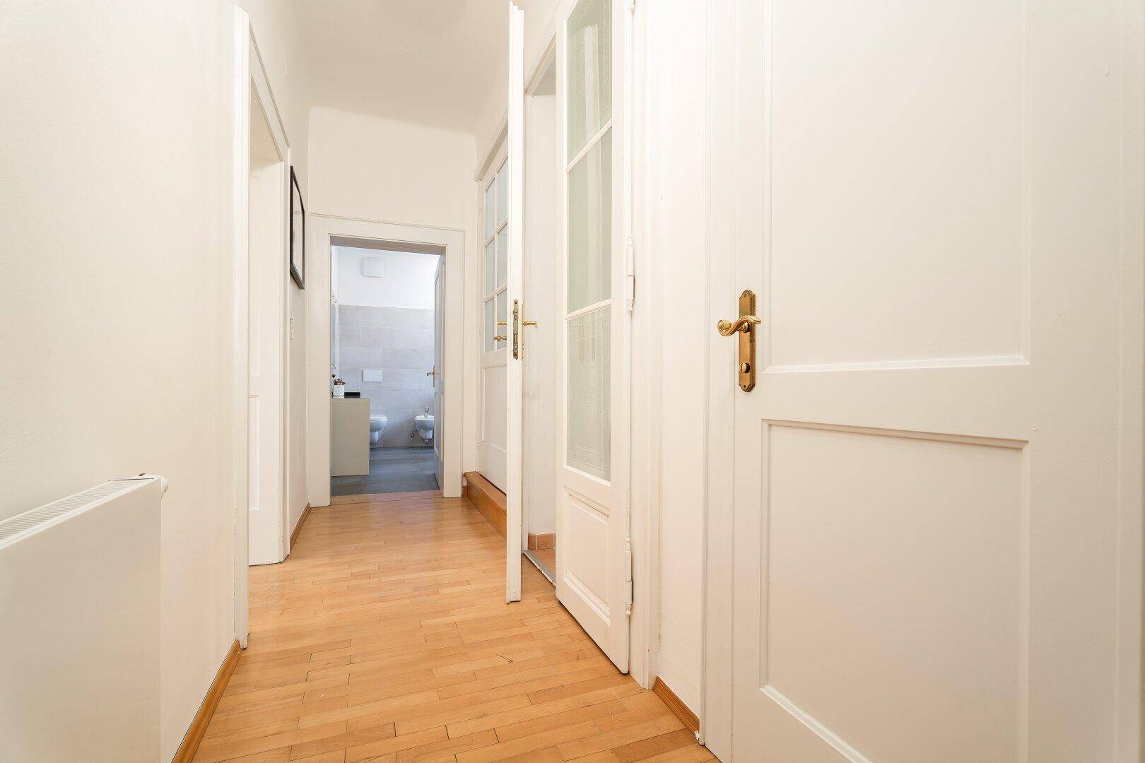Heller Flur mit Holzboden, weißen Türen und Blick in ein weiteres Zimmer.