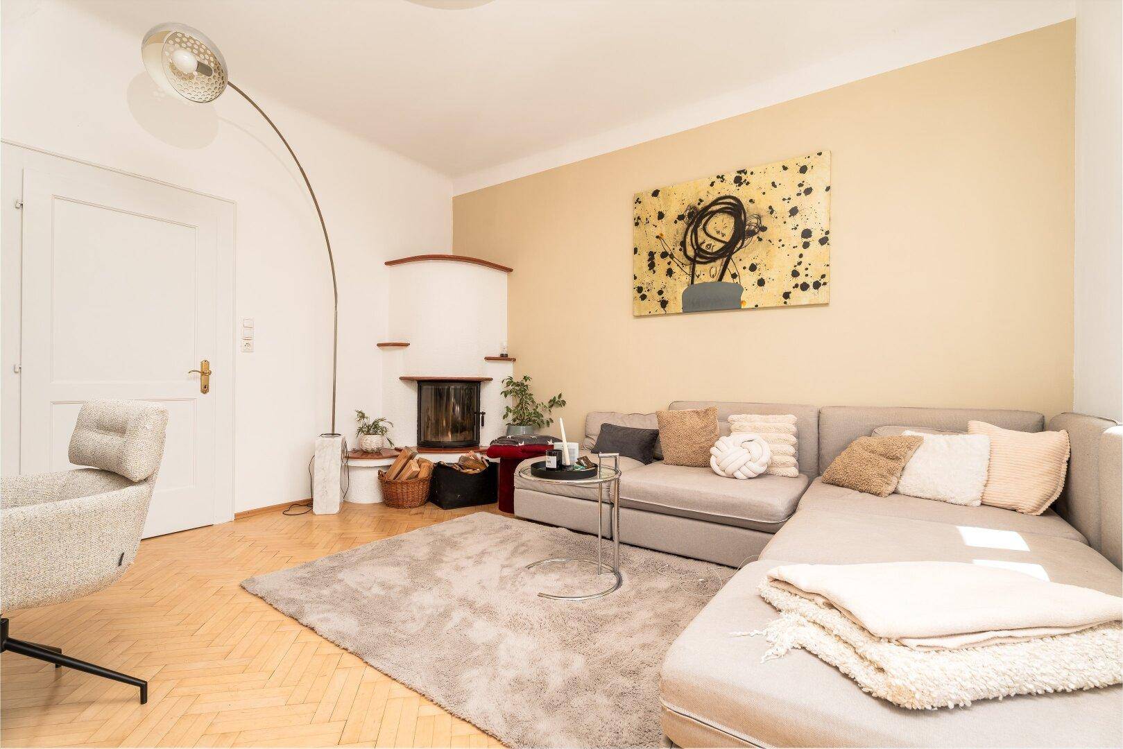 Gemütliches Wohnzimmer mit hellem Sofa, Fischgrätparkett und einem traditionellen Kamin.