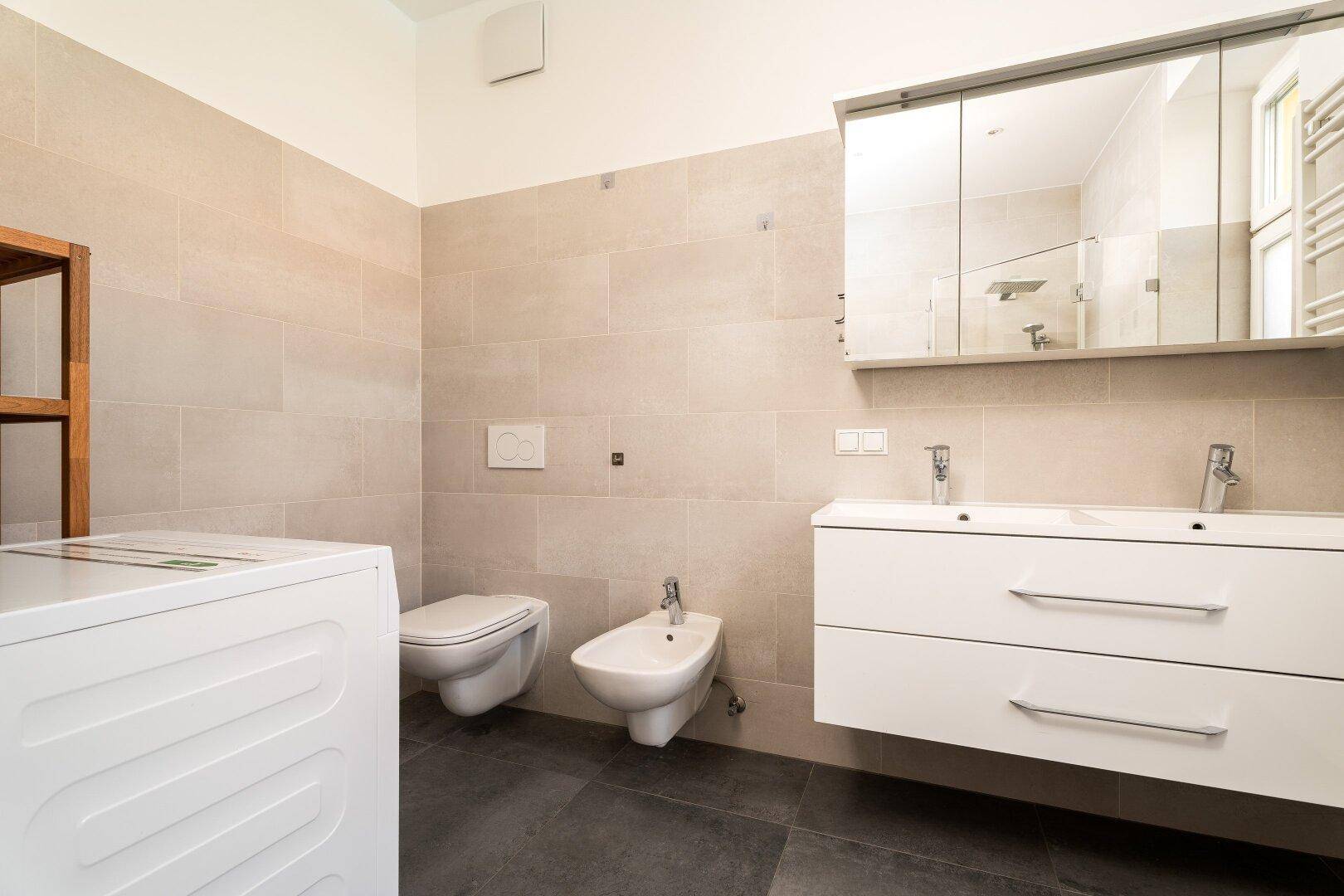 Geräumiges Badezimmer mit Toilette, Bidet, Doppelwaschbecken und Waschmaschine.