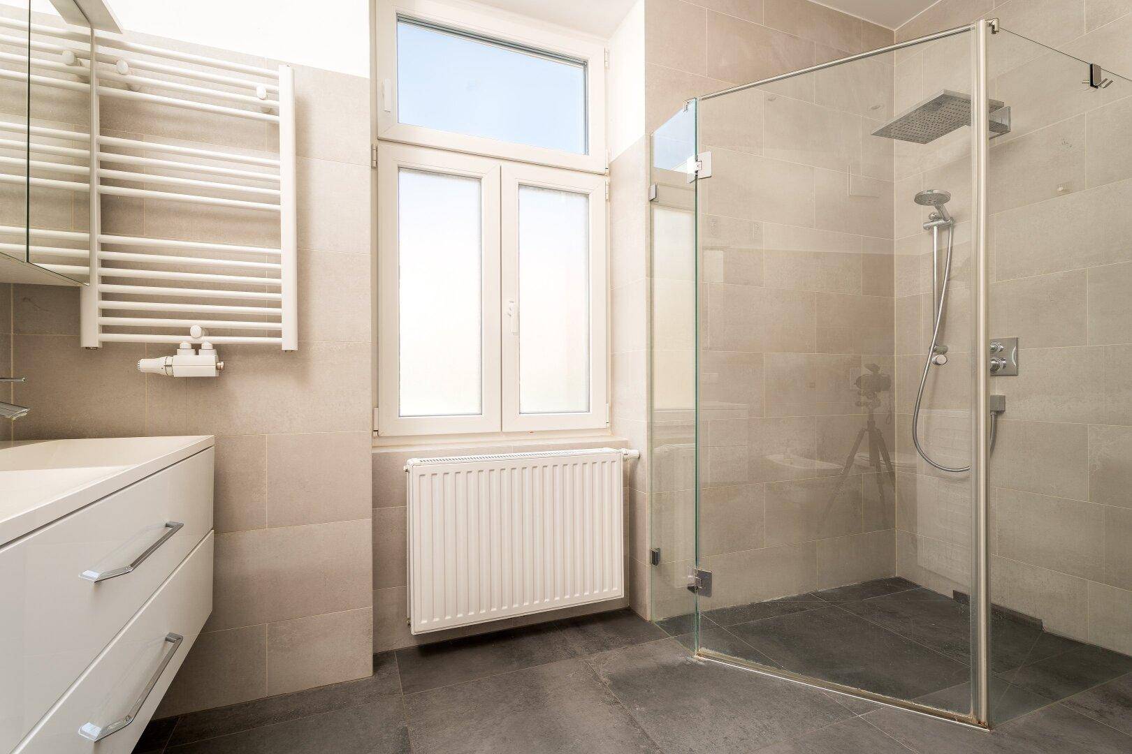 Modernes Badezimmer mit begehbarer Dusche, beheiztem Handtuchhalter und großem Fenster.