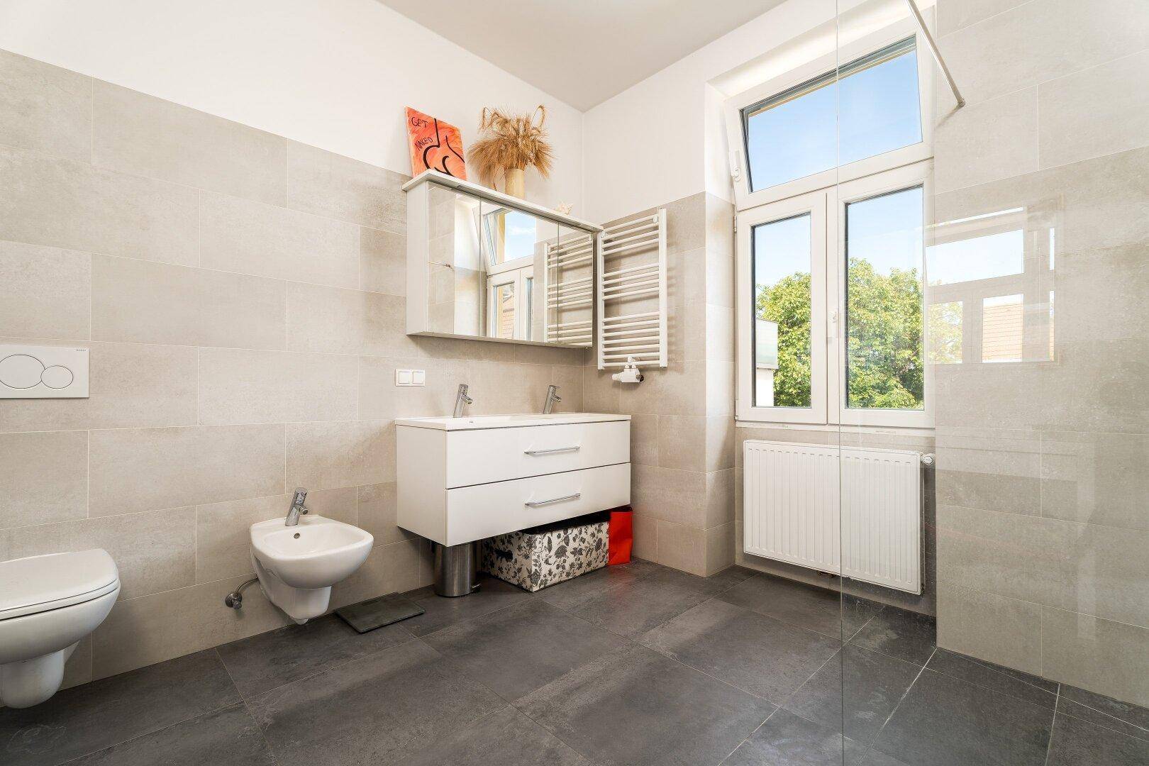 Helles Badezimmer mit Dusche, WC, Bidet und großem Fenster für viel Tageslicht.
