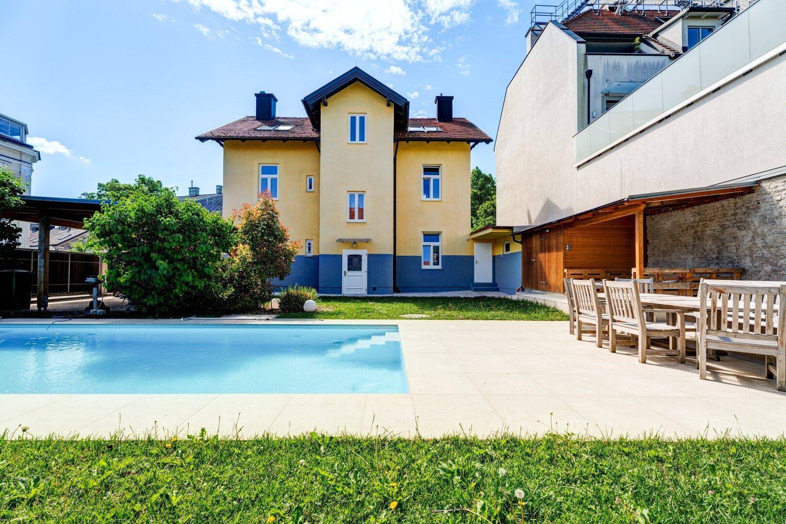 Außenansicht des Gebäudes mit Swimmingpool und gepflasterter Terrasse mit Esstisch im Garten.