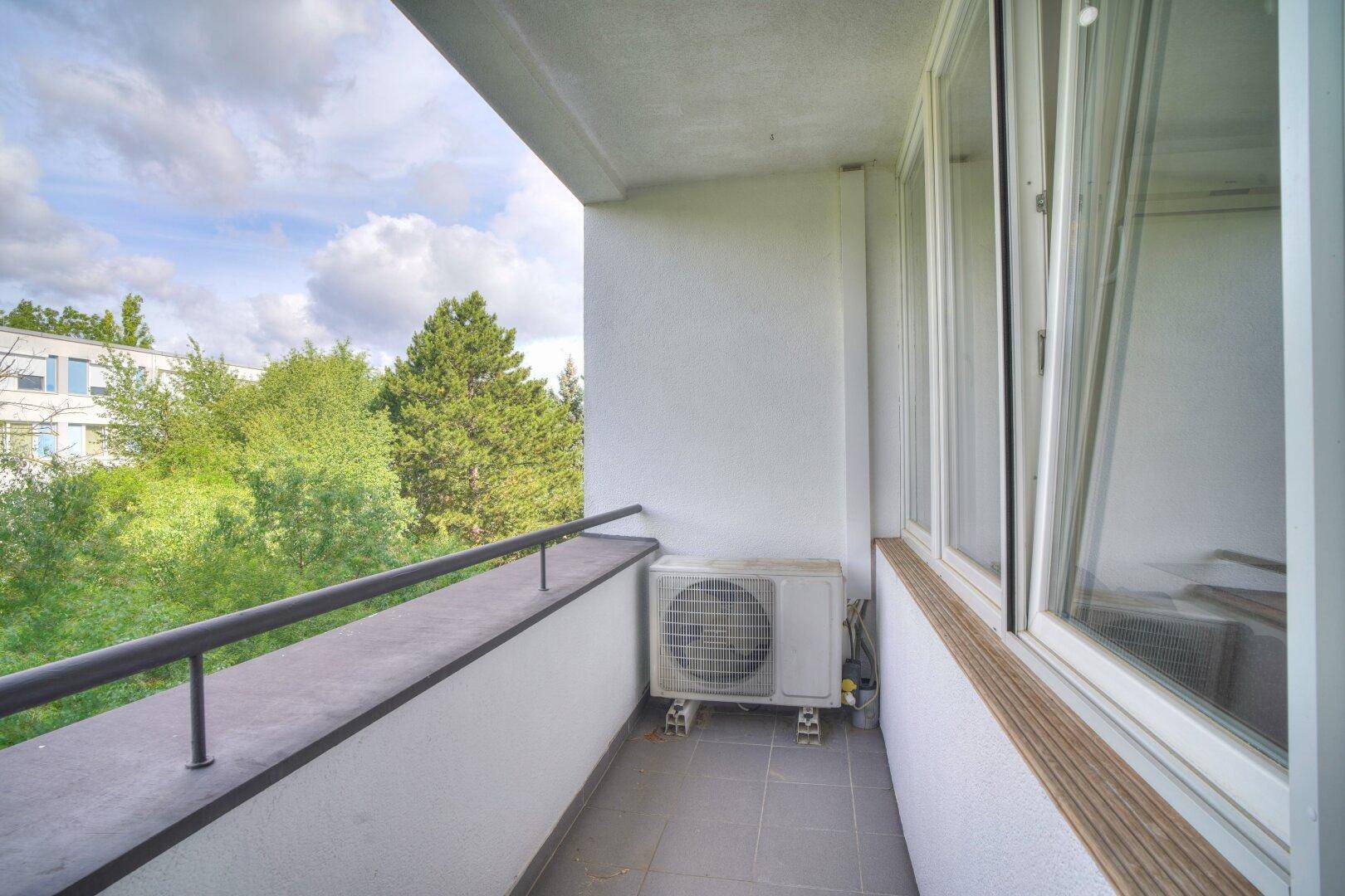 Schmaler Balkon mit Klimaanlage und Blick auf die grüne Umgebung.