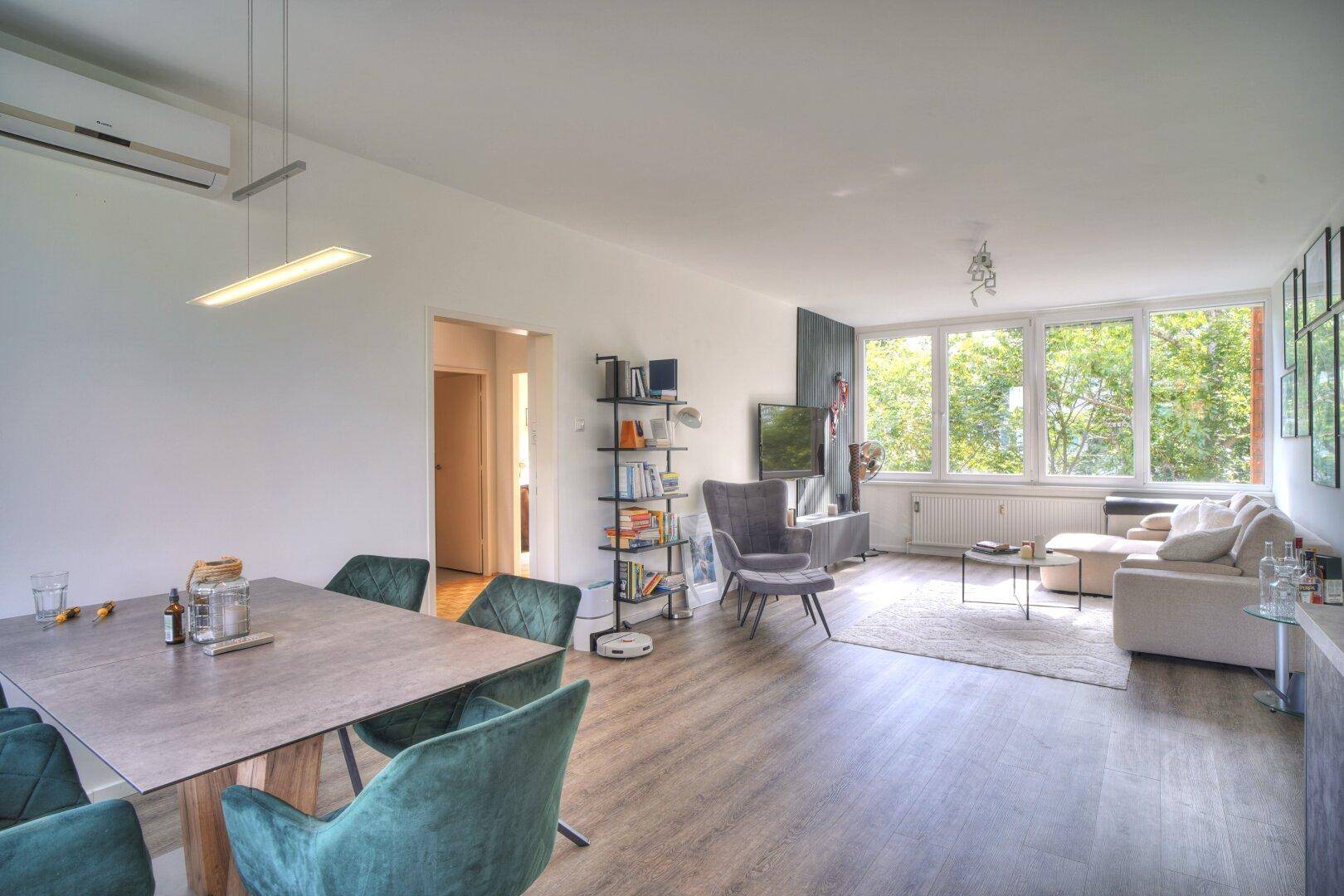 Heller Essbereich mit modernem Tisch, grünen Stühlen und offener Verbindung zum Wohnzimmer.