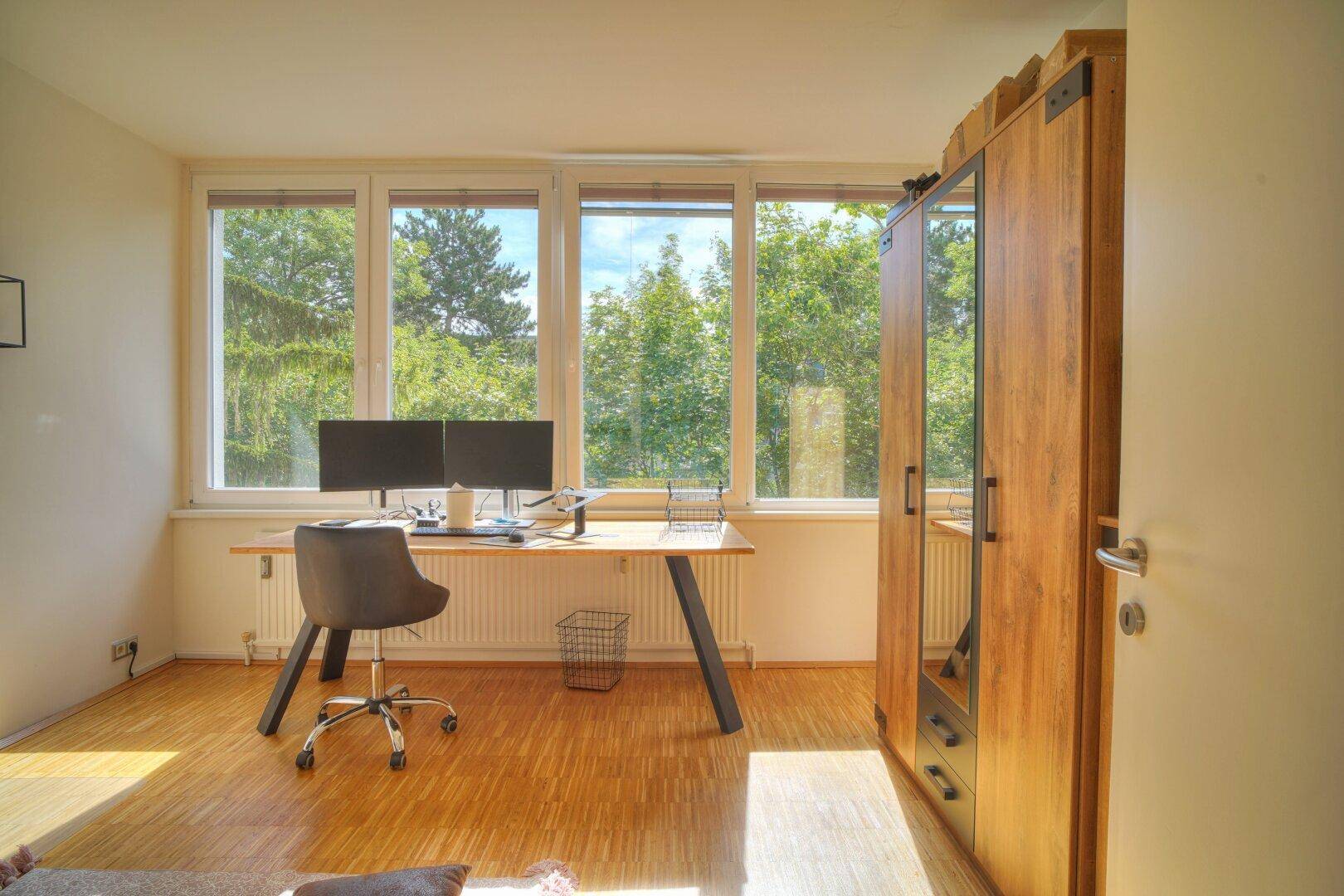 Arbeitszimmer mit Holzschrank, Schreibtisch und großen Fenstern für eine angenehme Arbeitsatmosphäre.