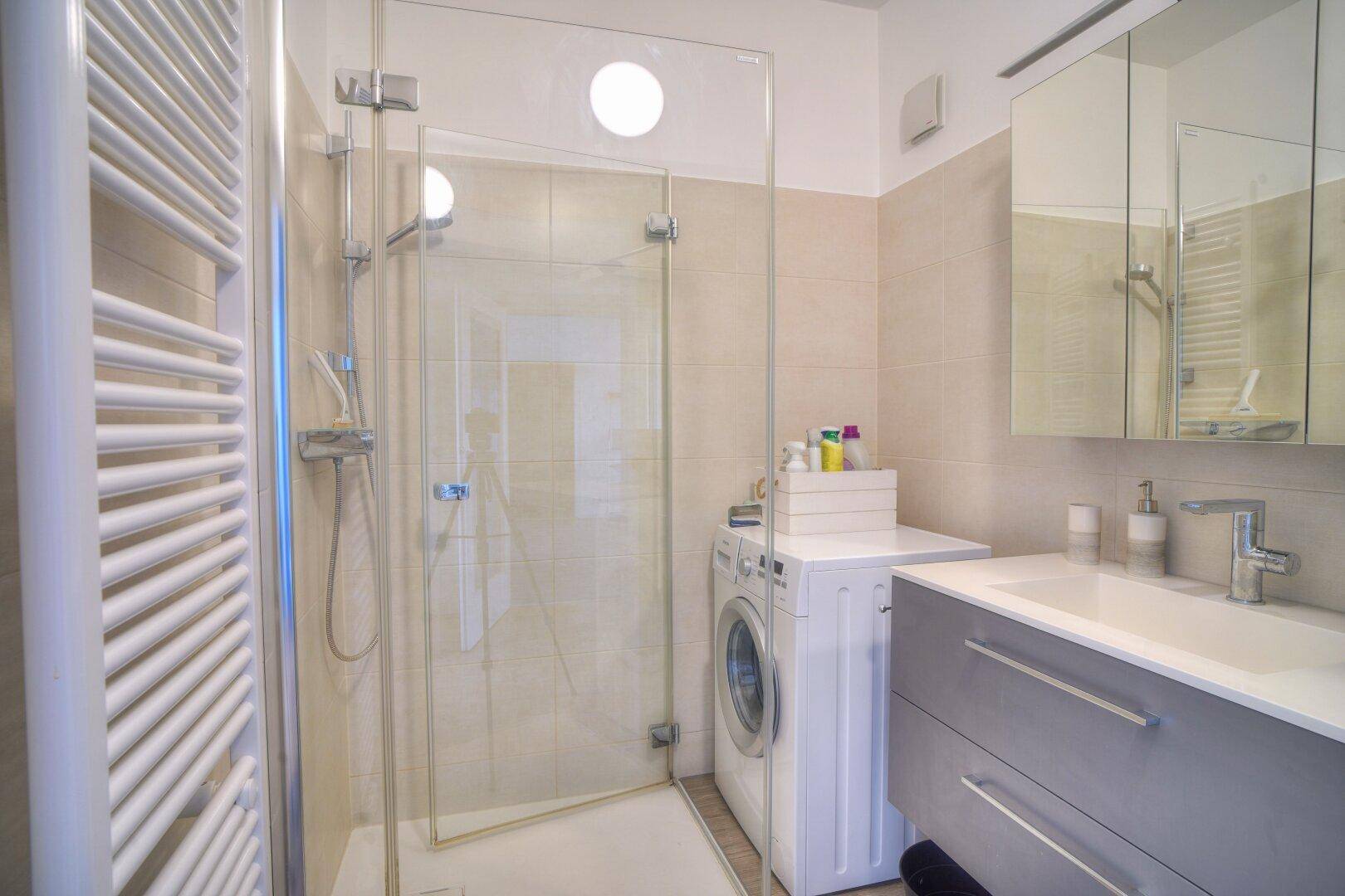 Modernes Badezimmer mit begehbarer Dusche, Waschbecken und integrierter Waschmaschine.