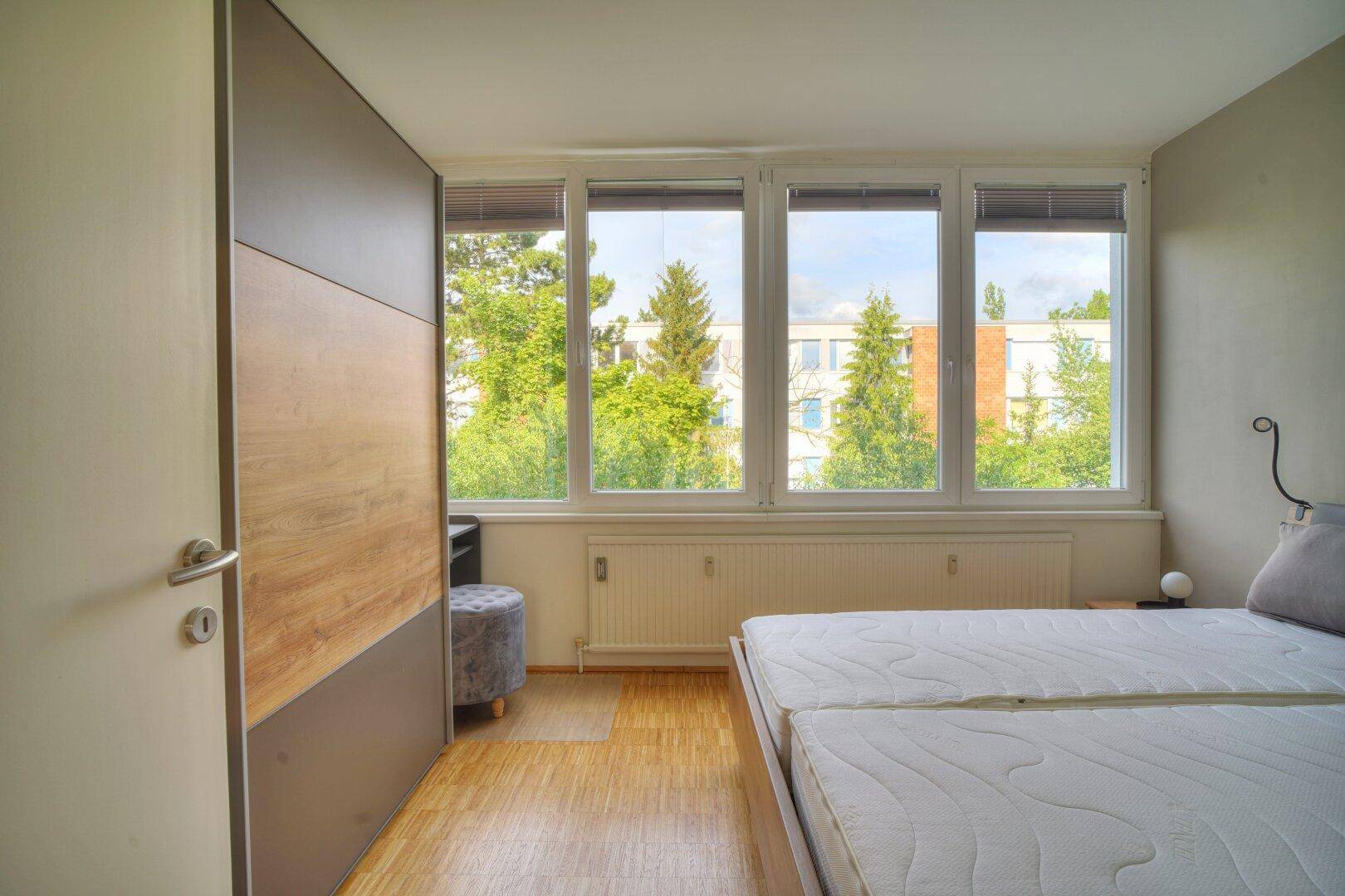 Schlafzimmer mit Holzfußboden, Einbauschrank und großen Fenstern für viel Tageslicht.