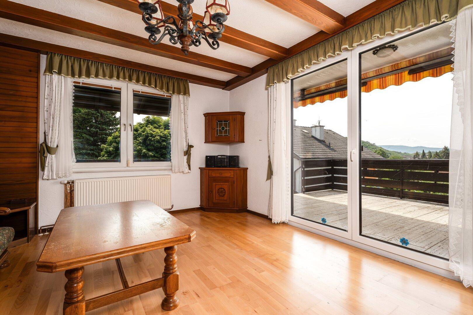Helles Wohnzimmer mit Holzbalkendecke und großem Fenster mit Balkonzugang.