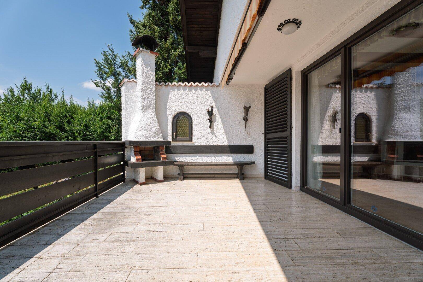 Sonnige Terrasse mit traditionellem Grill und Zugang zum Innenbereich des Hauses.