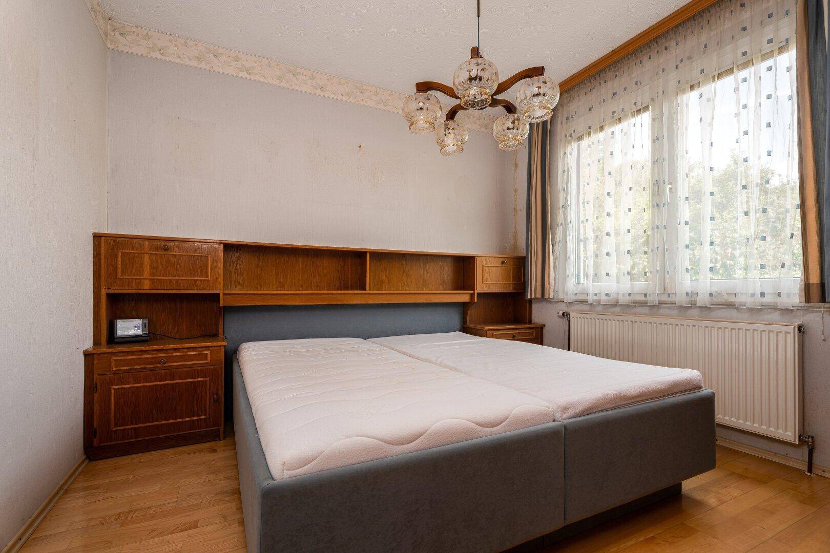 Schlafzimmer mit Doppelbett, Holzmöbeln und Fenster, das viel Tageslicht hereinlässt.
