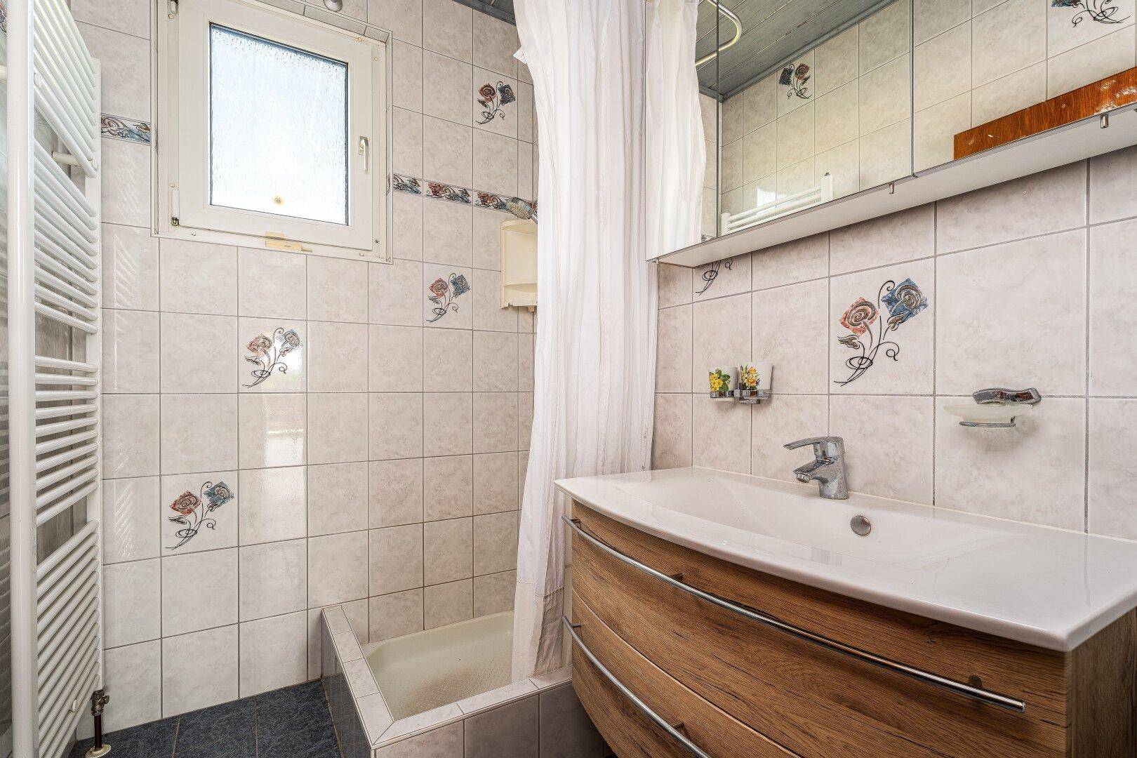 Badezimmer mit Waschbecken, Spiegelschrank, Badewanne mit Duschvorhang und gemusterten Fliesen.