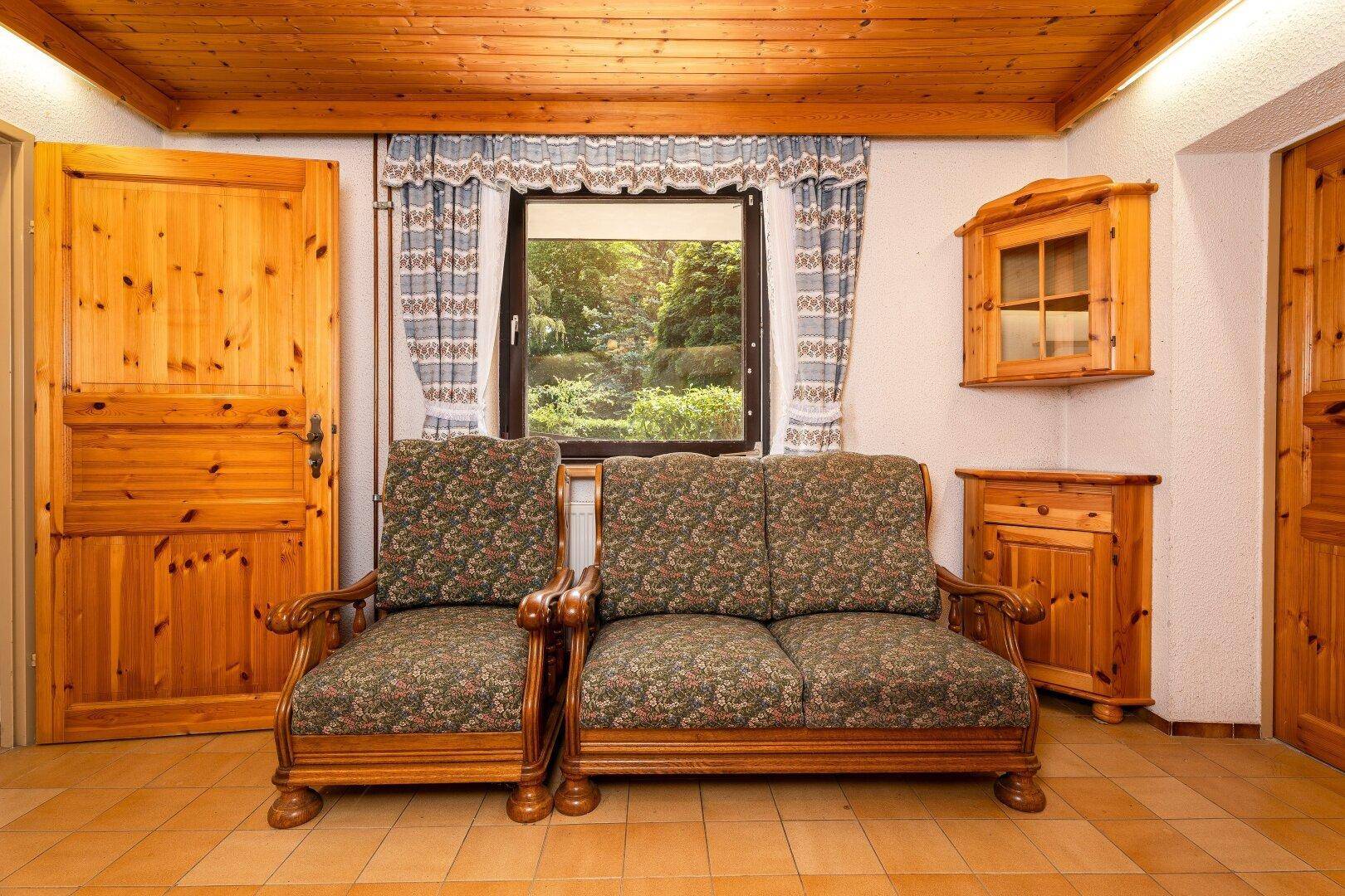 Gemütlicher Raum mit Holztäfelung, bequemen Sofas und Fenster mit Blick ins Grüne.