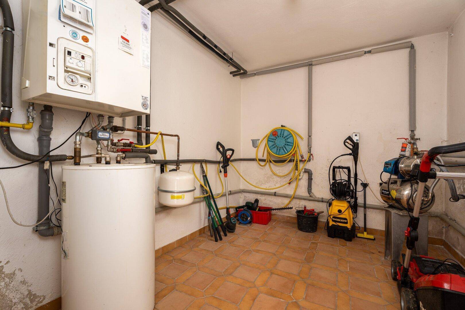 Hauswirtschaftsraum mit Heizungsanlage, Warmwasserspeicher und Fliesenboden, ideal für Lagerung und Technik.