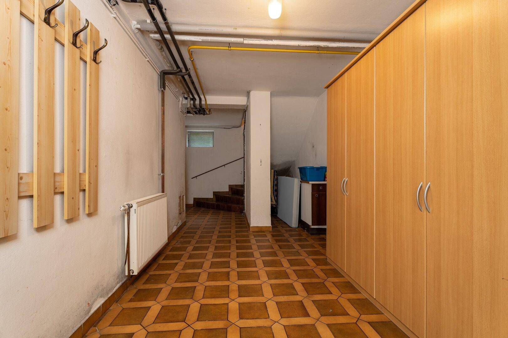 Kellerflur mit Einbauschränken, Heizkörper und Zugang zur Treppe, ausgestattet mit gemusterten Fliesen.