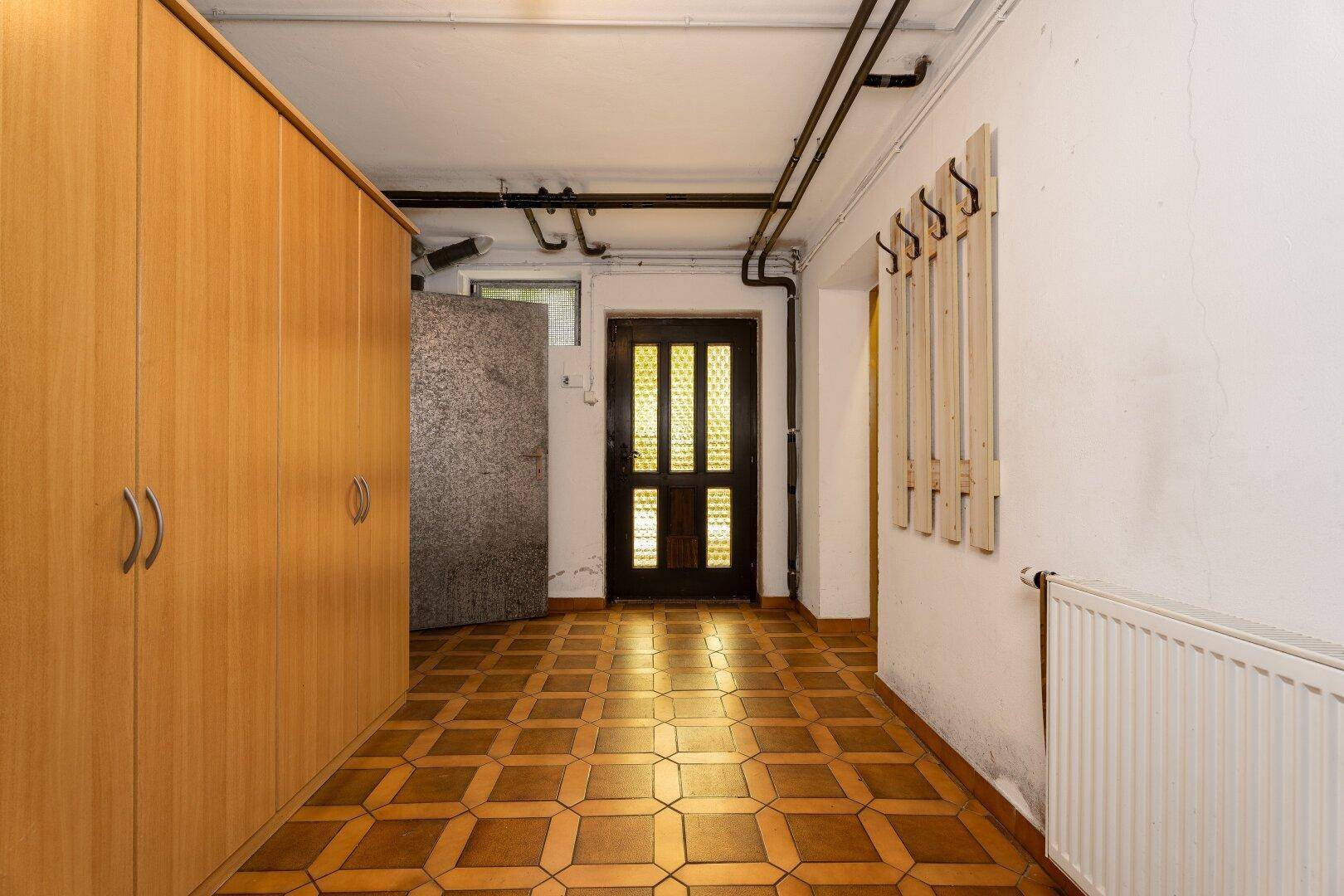 Heller Kellerflur mit Einbauschränken, Garderobe und Außentür, ausgestattet mit gemusterten Fliesen.