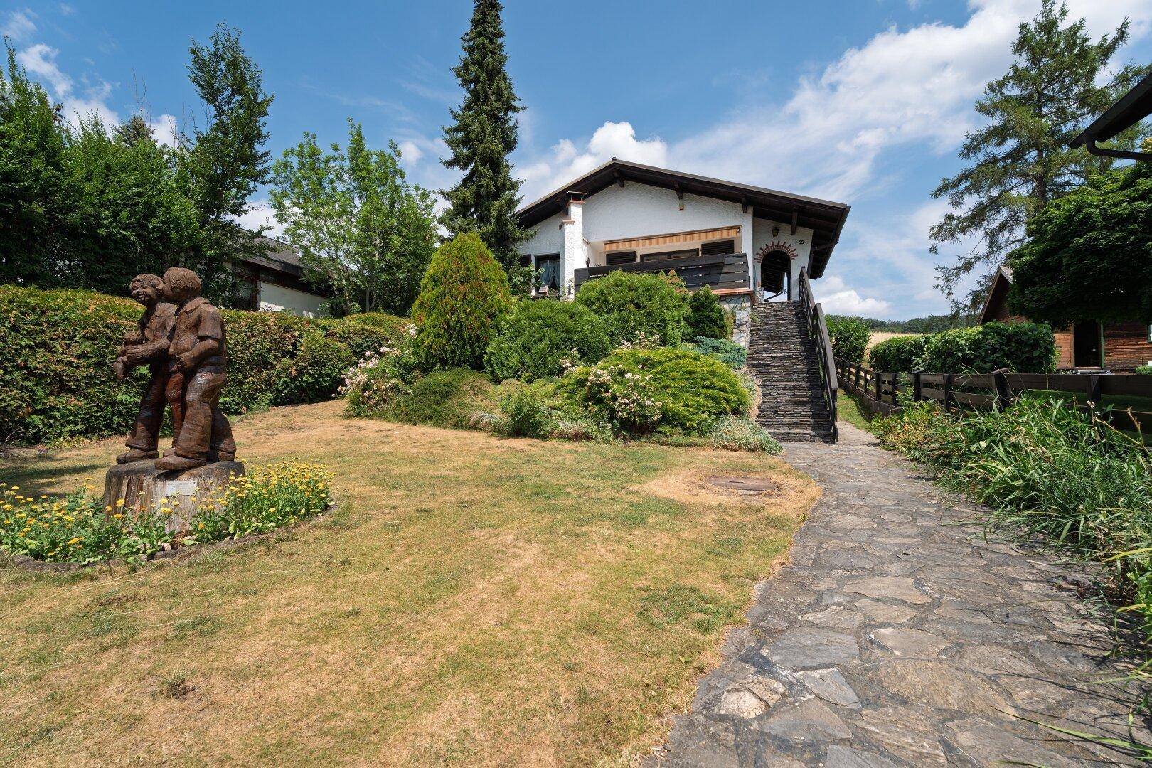 Vorderansicht des Hauses mit gepflegtem Garten, Steinweg und einer dekorativen Holzskulptur.