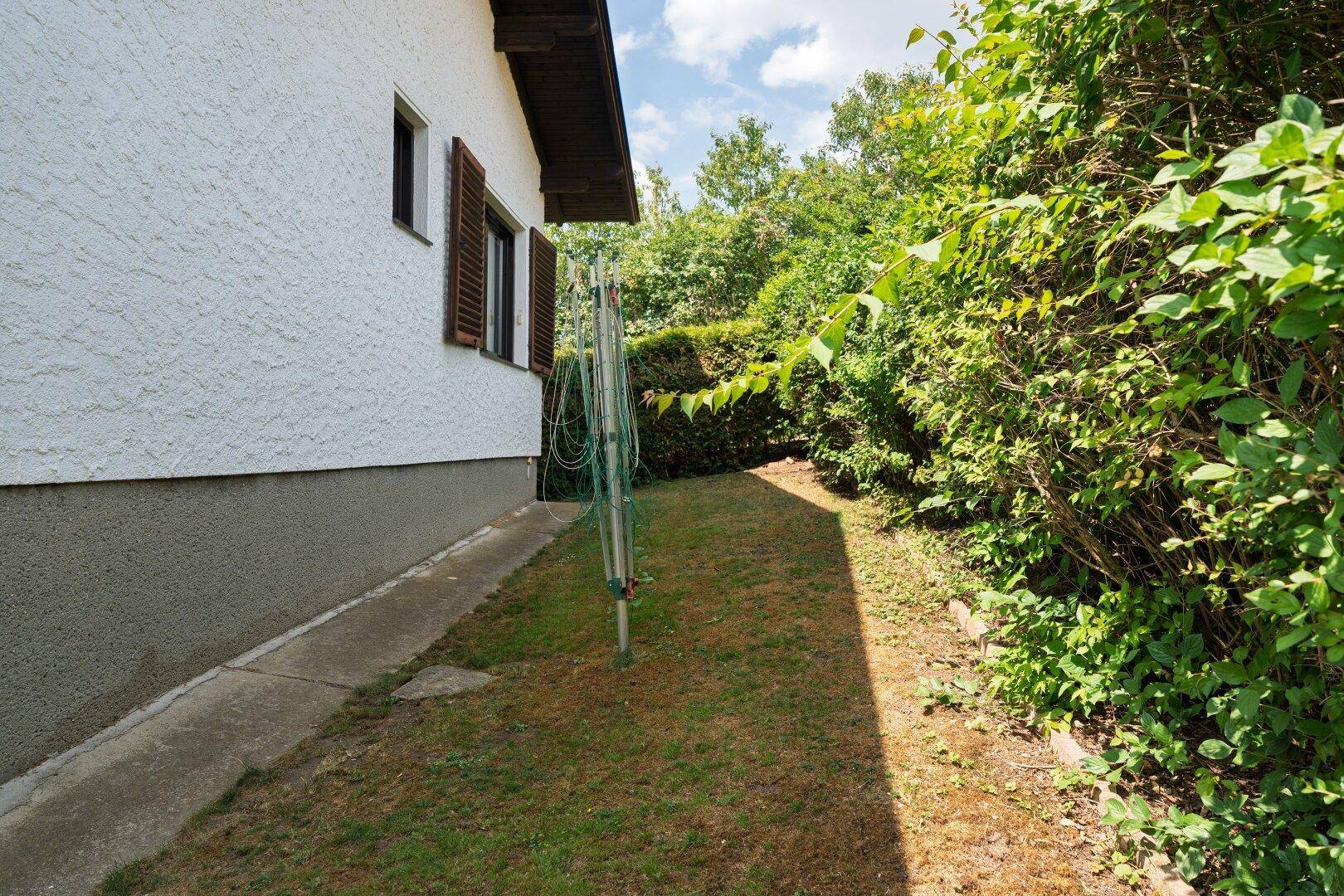 Seitlicher Gartenbereich des Hauses mit Rasenfläche, Hecke und einer Wäschespinne.