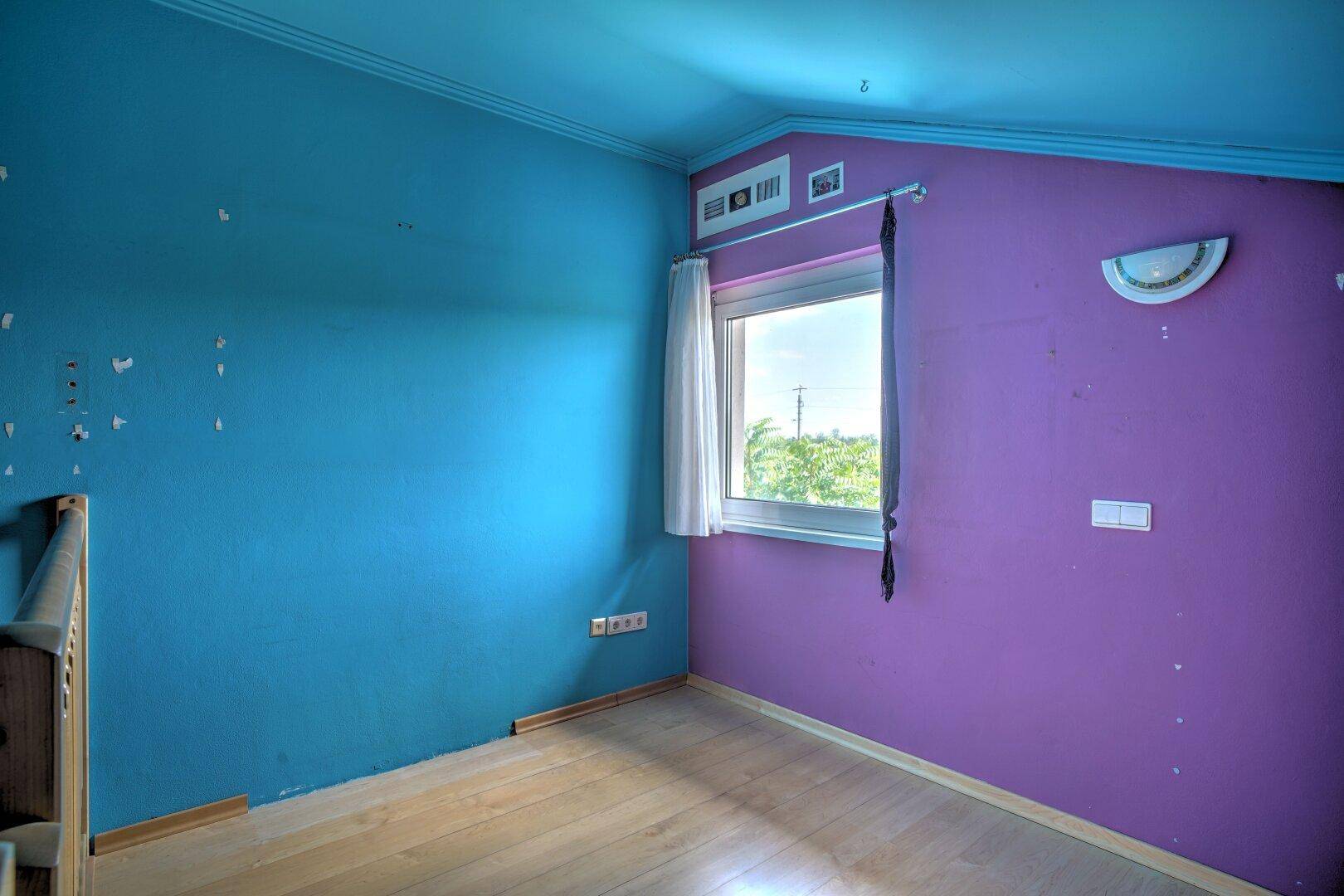 Buntes Zimmer mit Dachschräge, Fenster und Holzboden, ideal als Kinder- oder Gästezimmer.