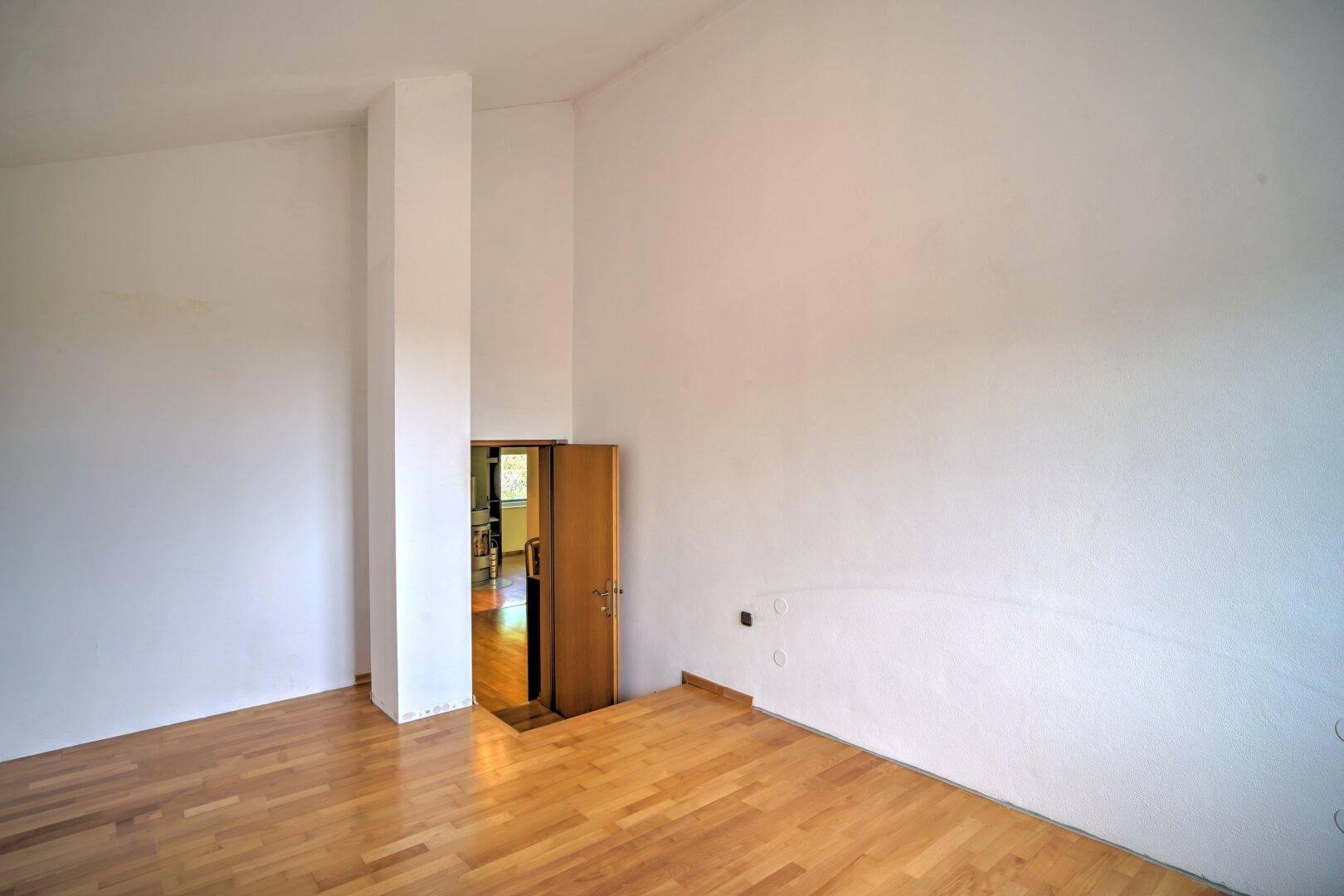 Leeres Zimmer mit Holzboden und weiß gestrichenen Wänden, bereit zur individuellen Gestaltung.