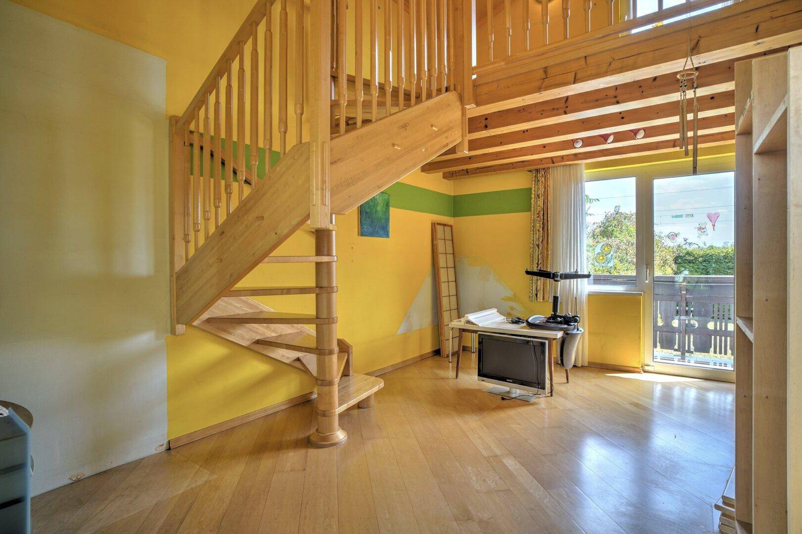 Helles Zimmer mit Holztreppe, Balkonzugang und lebhaften gelben Wänden.
