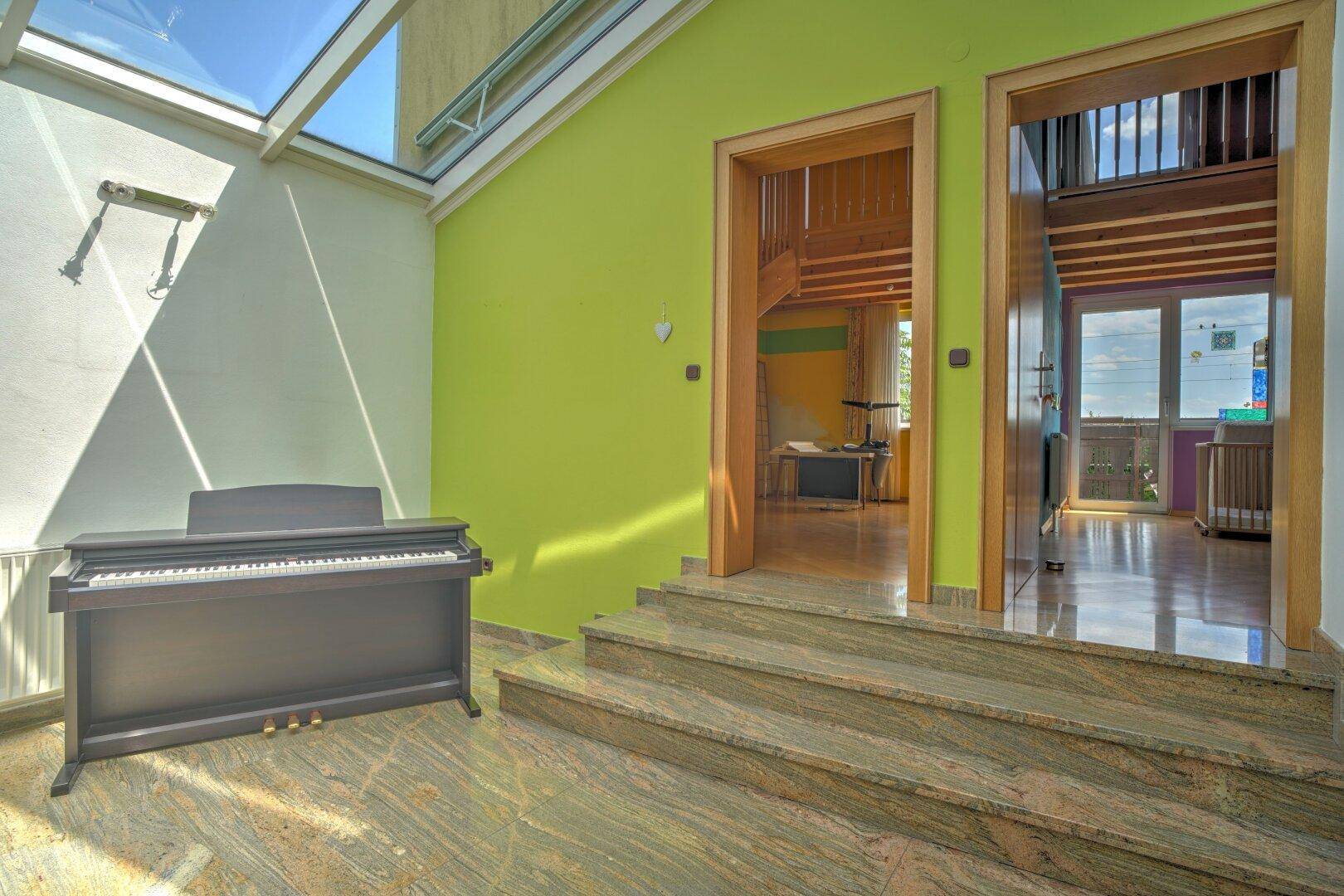 Heller Eingangsbereich mit Treppe, Klavier und farbigen Wänden.