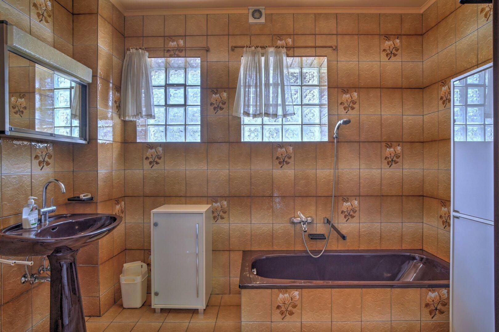 Badezimmer im 80er-Jahre-Stil mit braunen Fliesen, Badewanne und Waschbecken.
