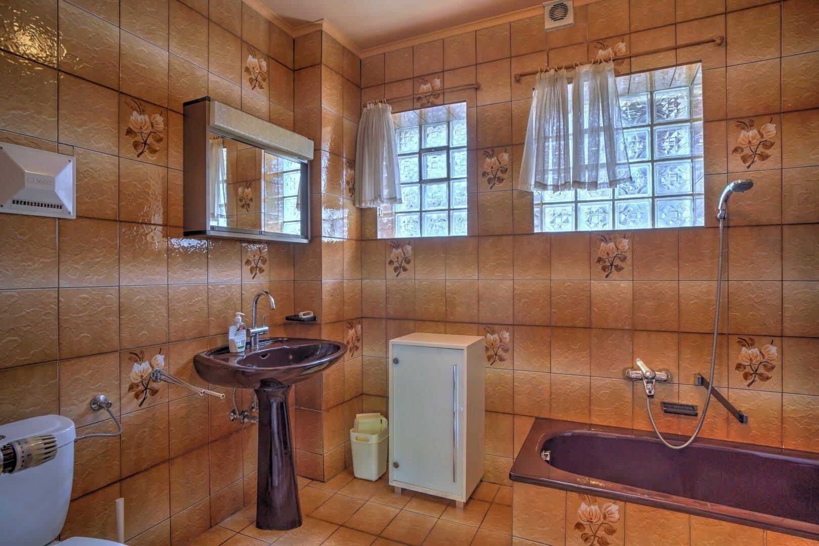 Retro-Badezimmer mit braunen Fliesen, Badewanne, Waschbecken und WC.