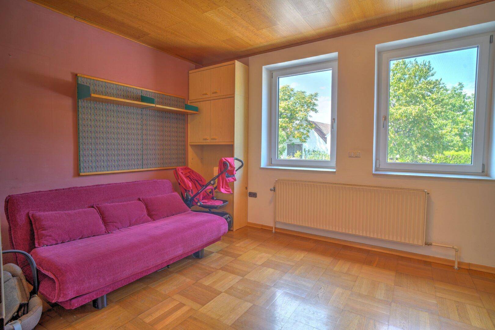 Schlafzimmer mit rosa Schlafsofa, Holzdecke und Blick ins Grüne.