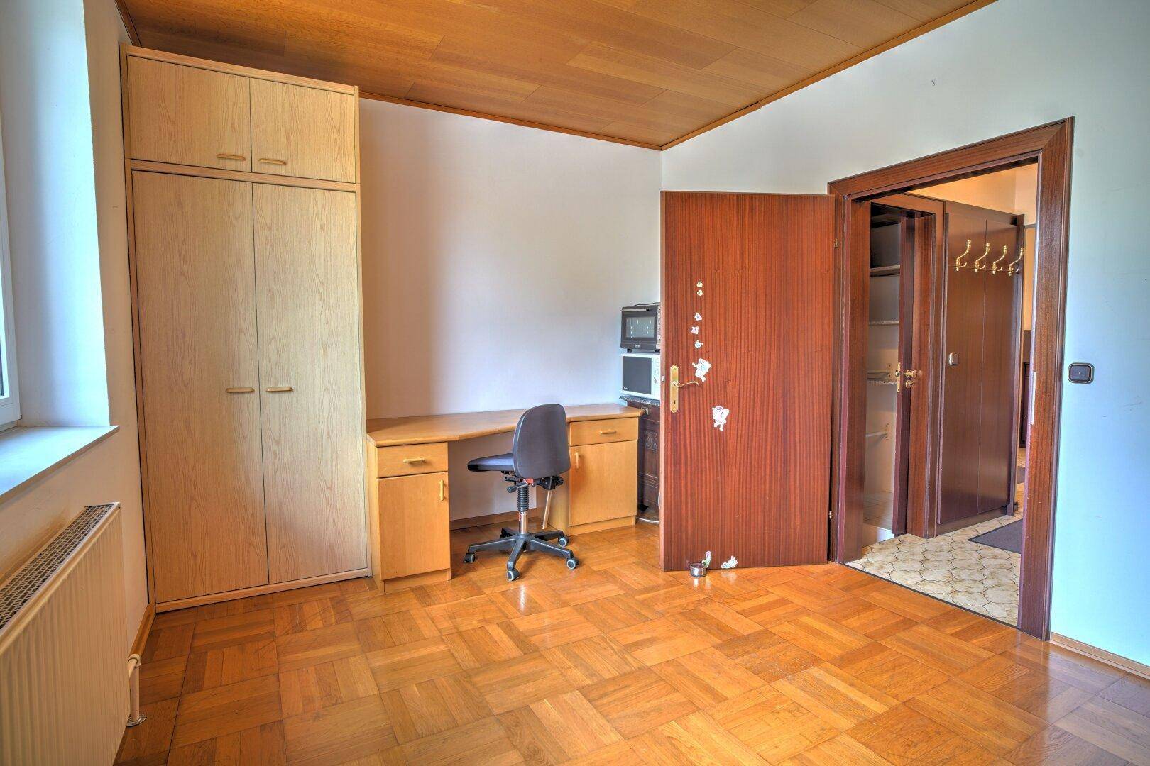 Arbeitszimmer mit Schreibtisch, Einbauschrank und Holzboden.