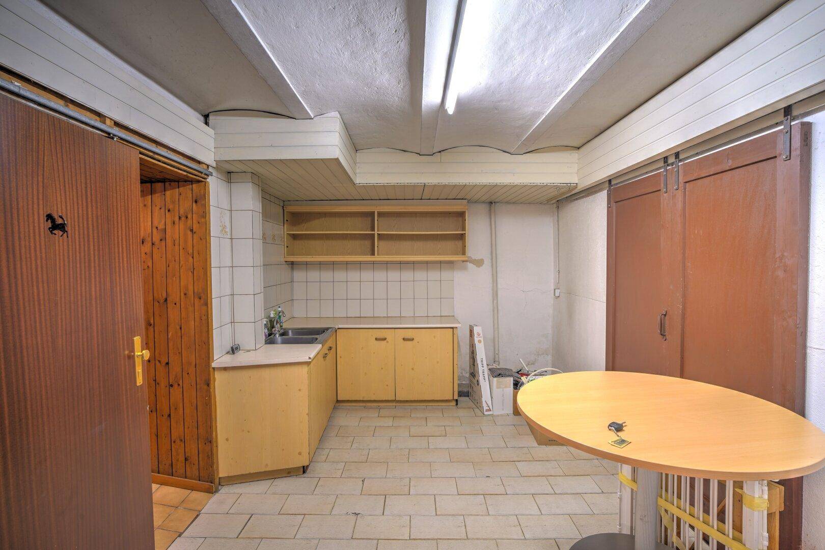 Kellerraum mit einfacher Küchenzeile, Fliesenboden und Stauraum.