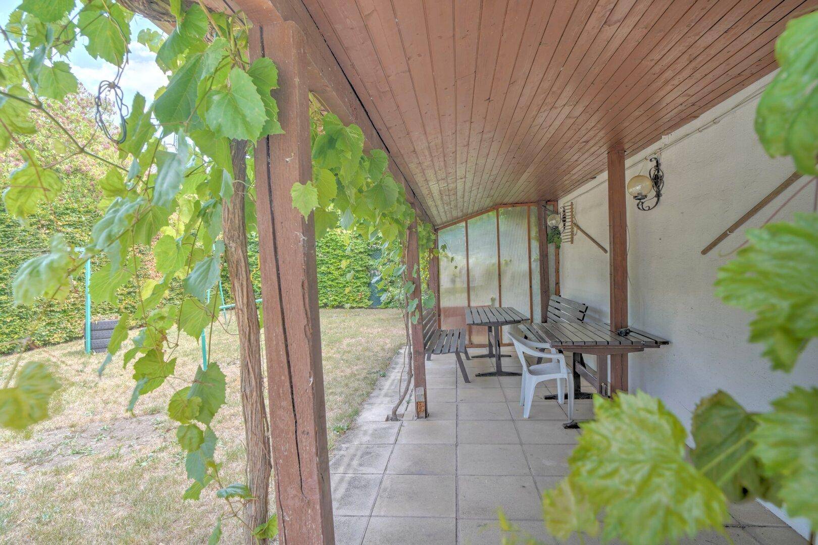 Überdachte Terrasse mit Holzbalken, Sitzgelegenheiten und Blick ins Grüne.