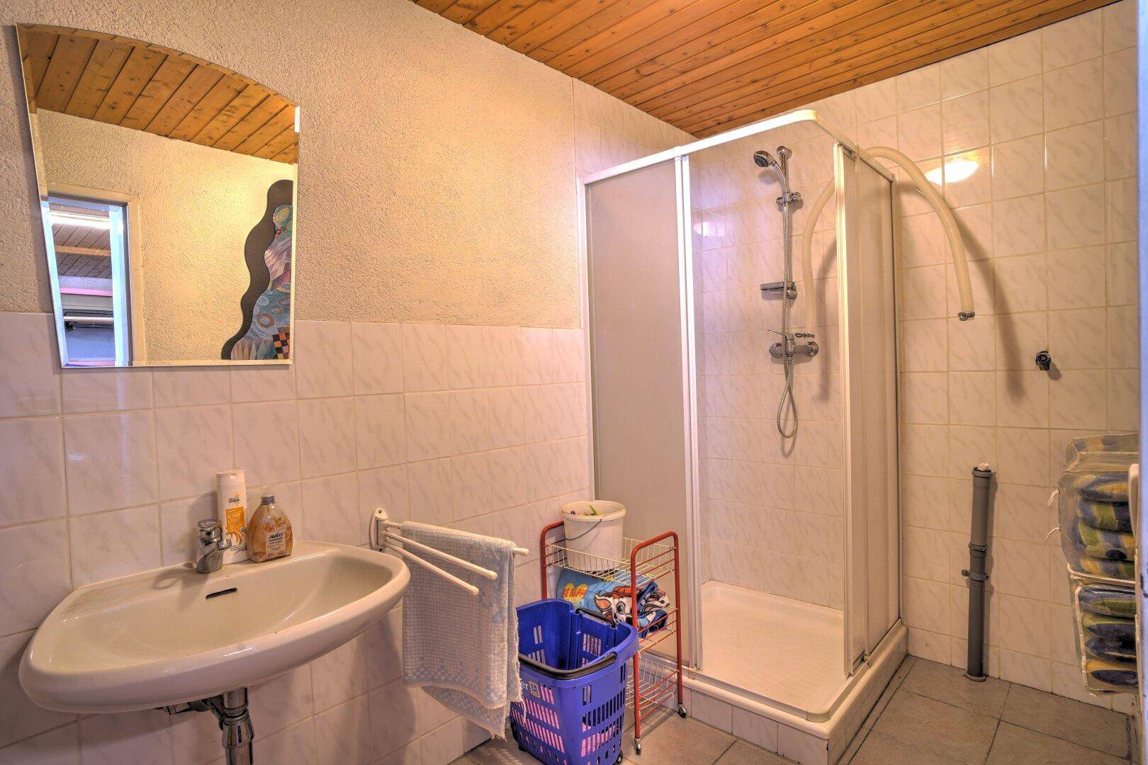 Badezimmer mit Duschkabine, Waschbecken und Holzdeckenverkleidung.