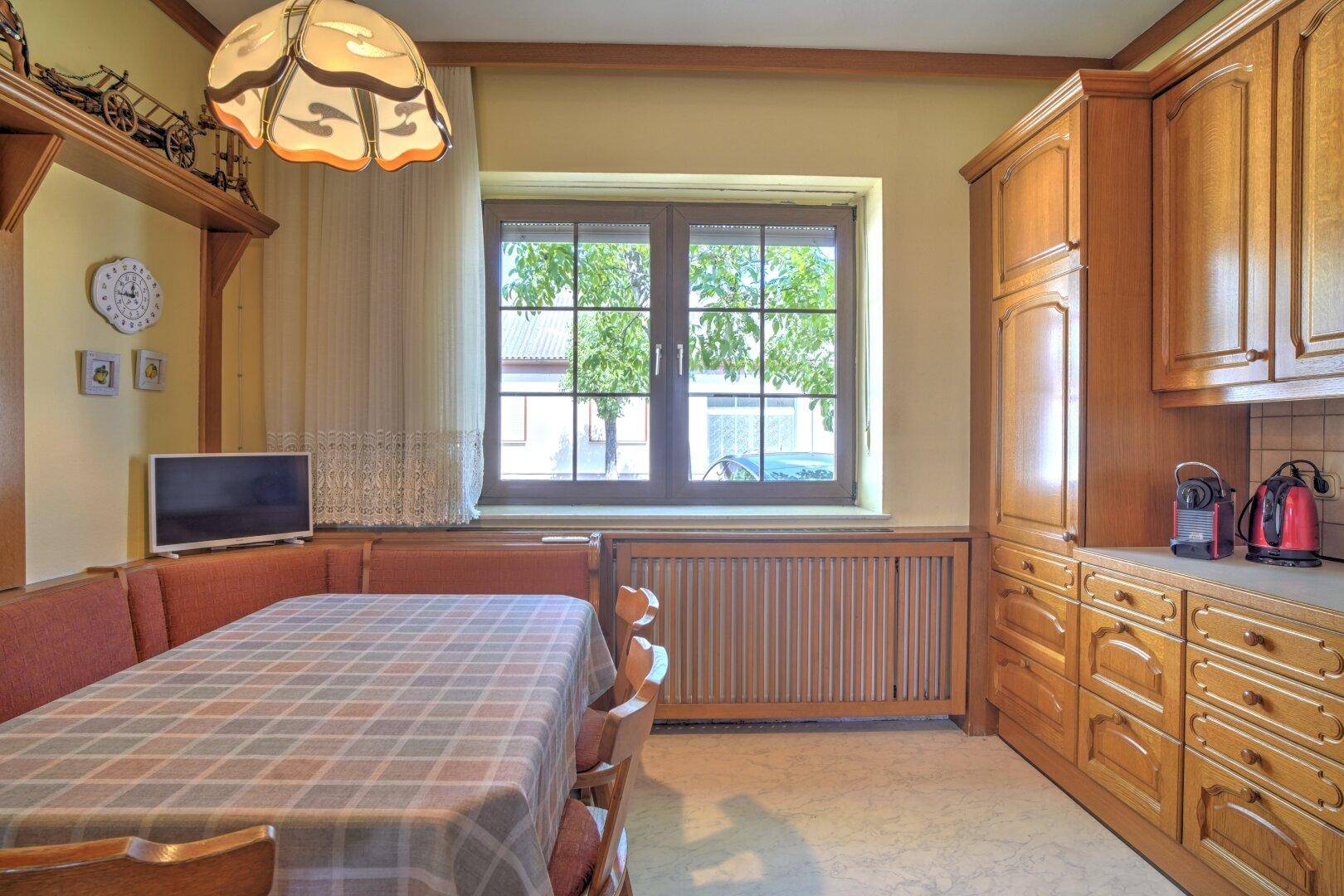 Gemütlicher Essbereich in der Holzküche mit karierter Tischdecke und Blick durch das Fenster.