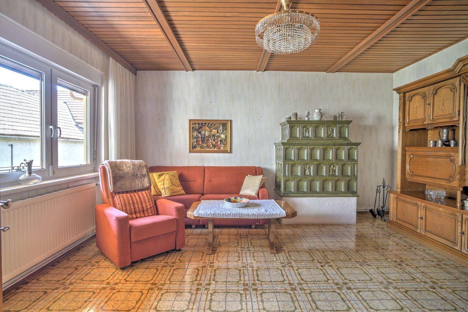 Gemütliches Wohnzimmer mit Kachelofen, Holzdecke und traditionellen Möbeln, hell gefliest.