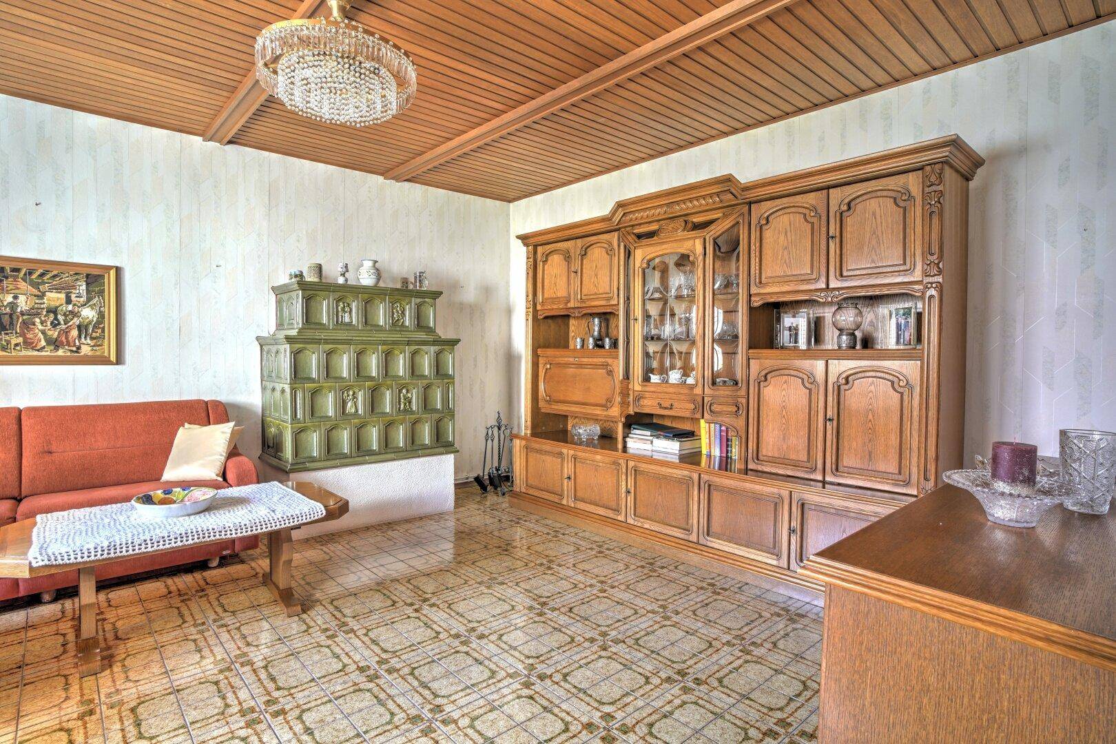 Traditionelles Wohnzimmer mit großem Holzschrank, Kachelofen und gemustertem Fliesenboden.