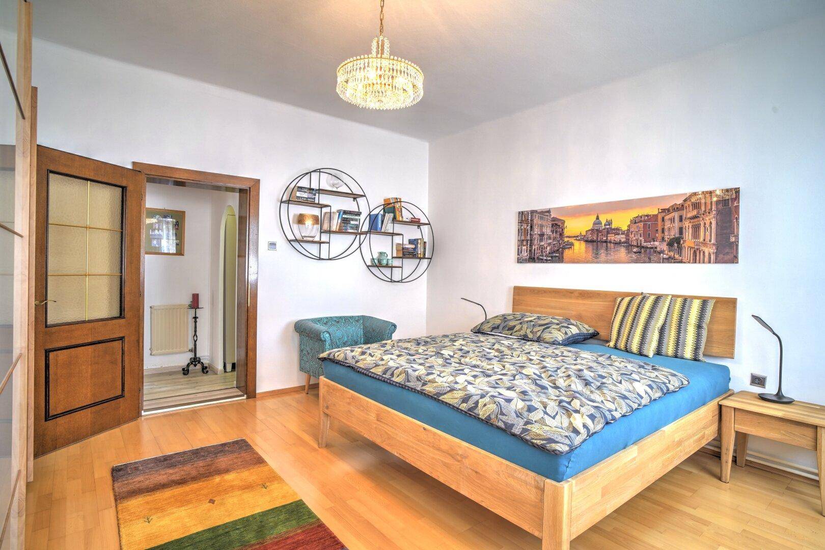 Modernes Schlafzimmer mit Holzbett, Parkettboden und farbenfrohem Teppich, hell und einladend.