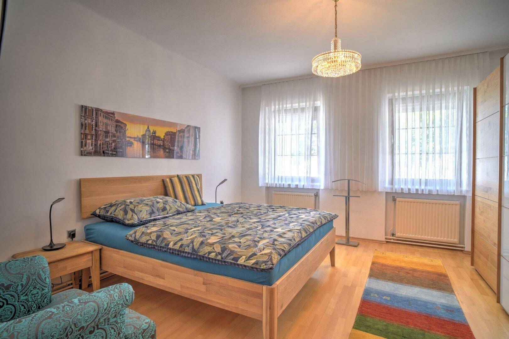 Helles Schlafzimmer mit zwei Fenstern, Holzbett und Parkettboden, modern und komfortabel eingerichtet.