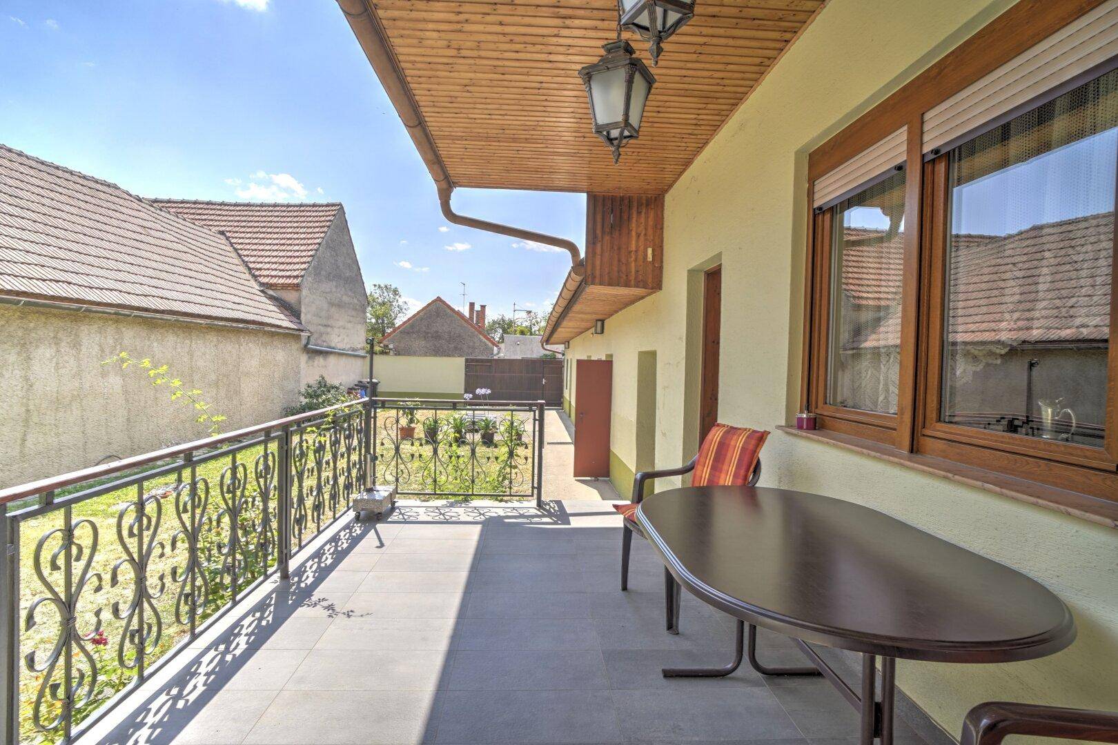 Überdachter Balkon mit schmiedeeisernem Geländer und Sitzgelegenheiten, bietet Blick auf den Garten.