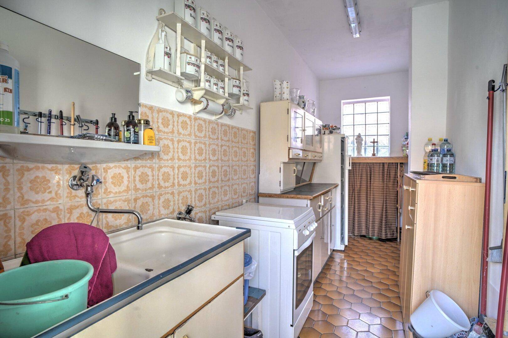 Funktionale Waschküche mit Spülbecken, Regalen und Fenster, bietet praktischen Arbeitsbereich.