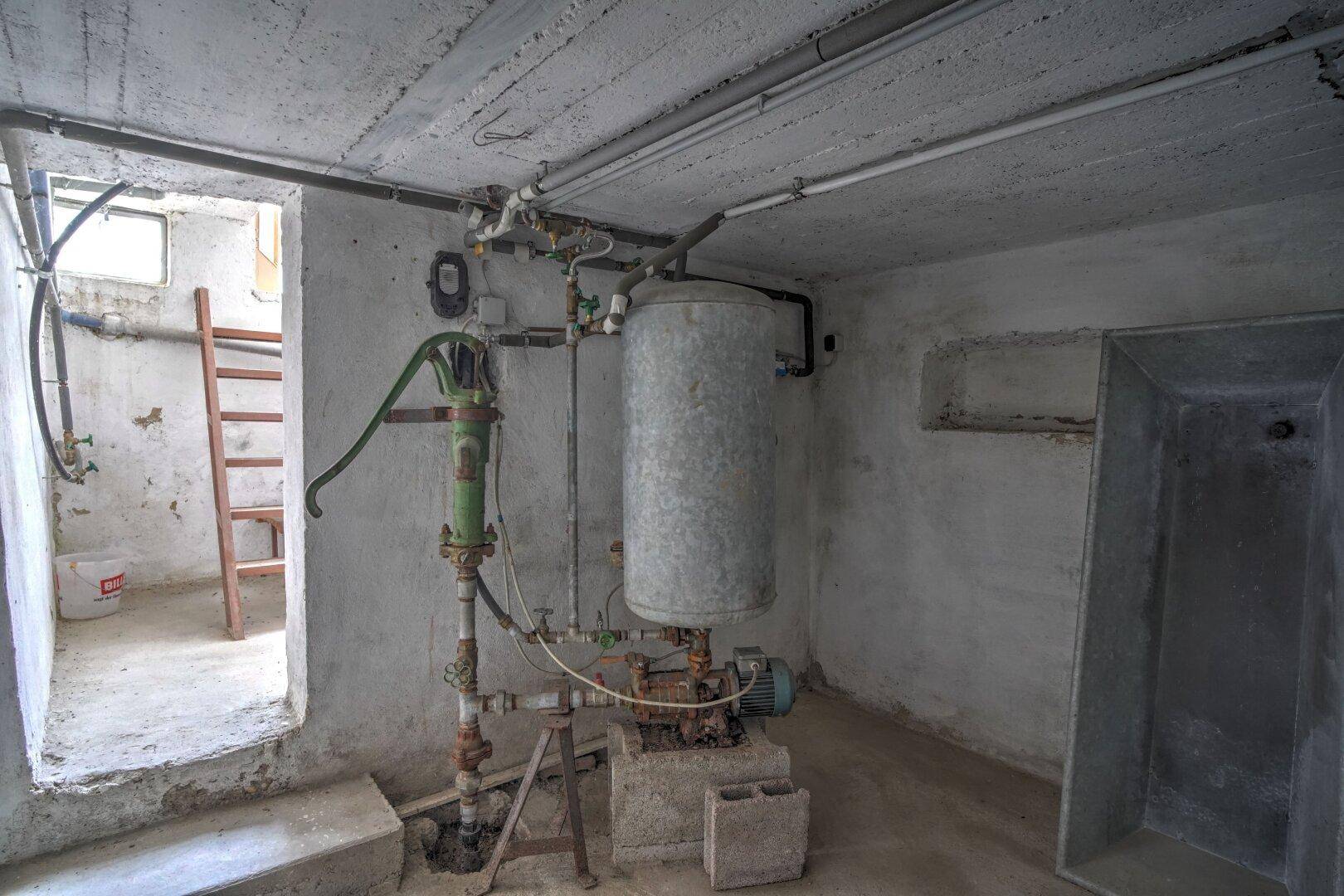 Unausgebauter Kellerraum mit Wasserboiler und Rohren, zeigt die technische Ausstattung.