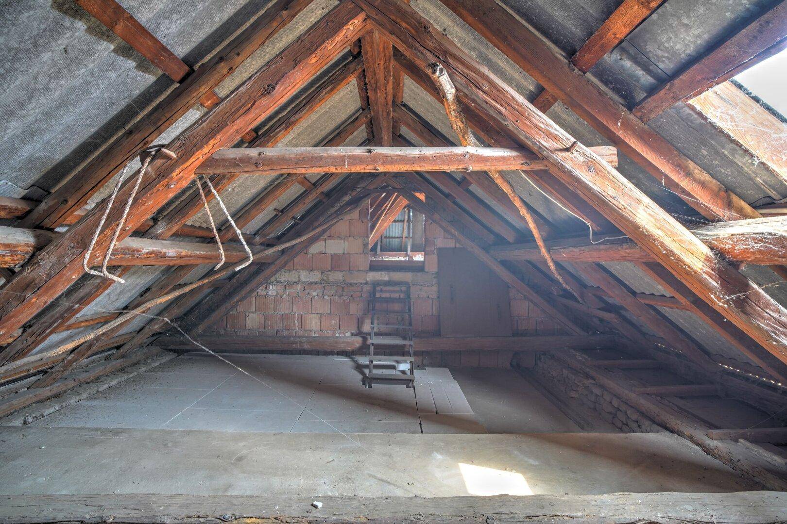 Unausgebauter Dachboden mit sichtbarer Holzkonstruktion und Ziegelwänden, bietet Ausbaupotenzial.